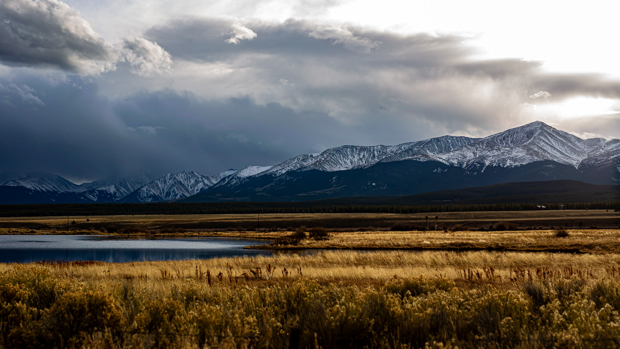 Landscape with mountains, cloudy sky, a body of water, and grassy plains in foreground.