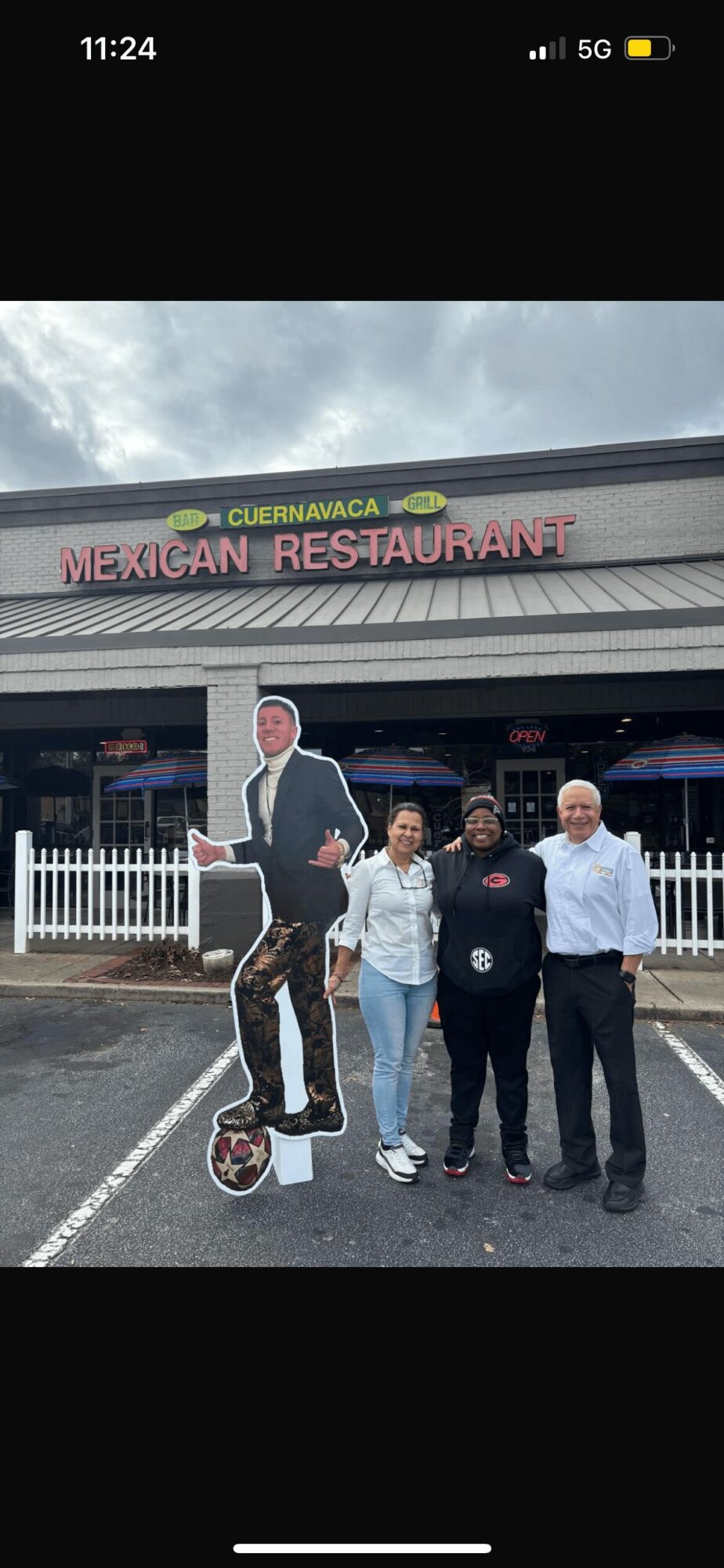Four people standing in front of a Mexican restaurant with a sign and a cardboard cutout of a man on a scooter.