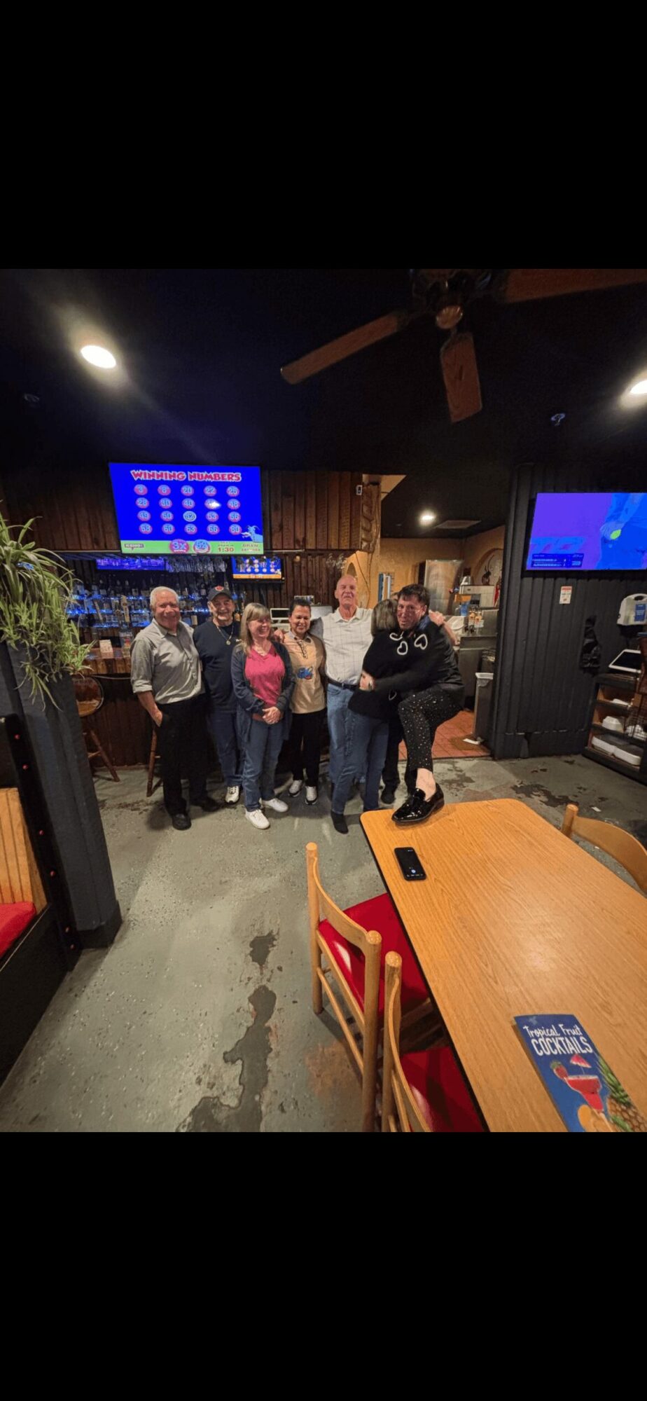 Group of people standing together in a restaurant or bar with digital screens on the wall.