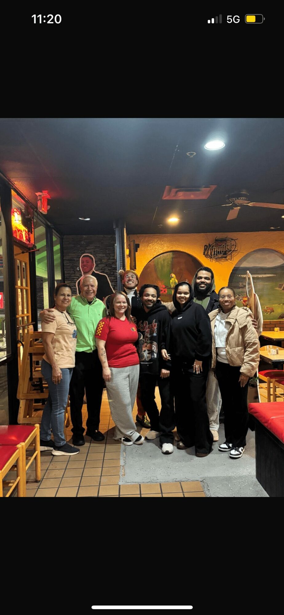 Group of nine people standing together in a colorful indoor setting, smiling at the camera.
