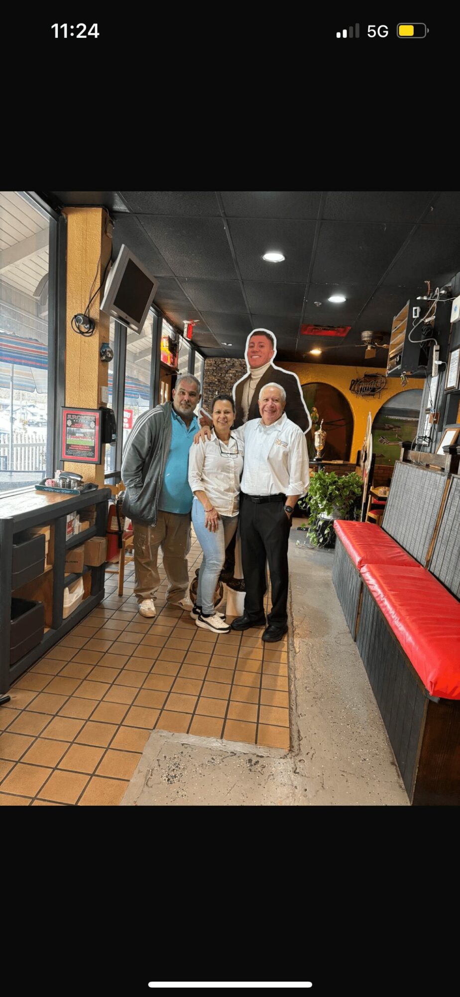 Four people standing inside a restaurant, smiling, with a bar and television behind them.