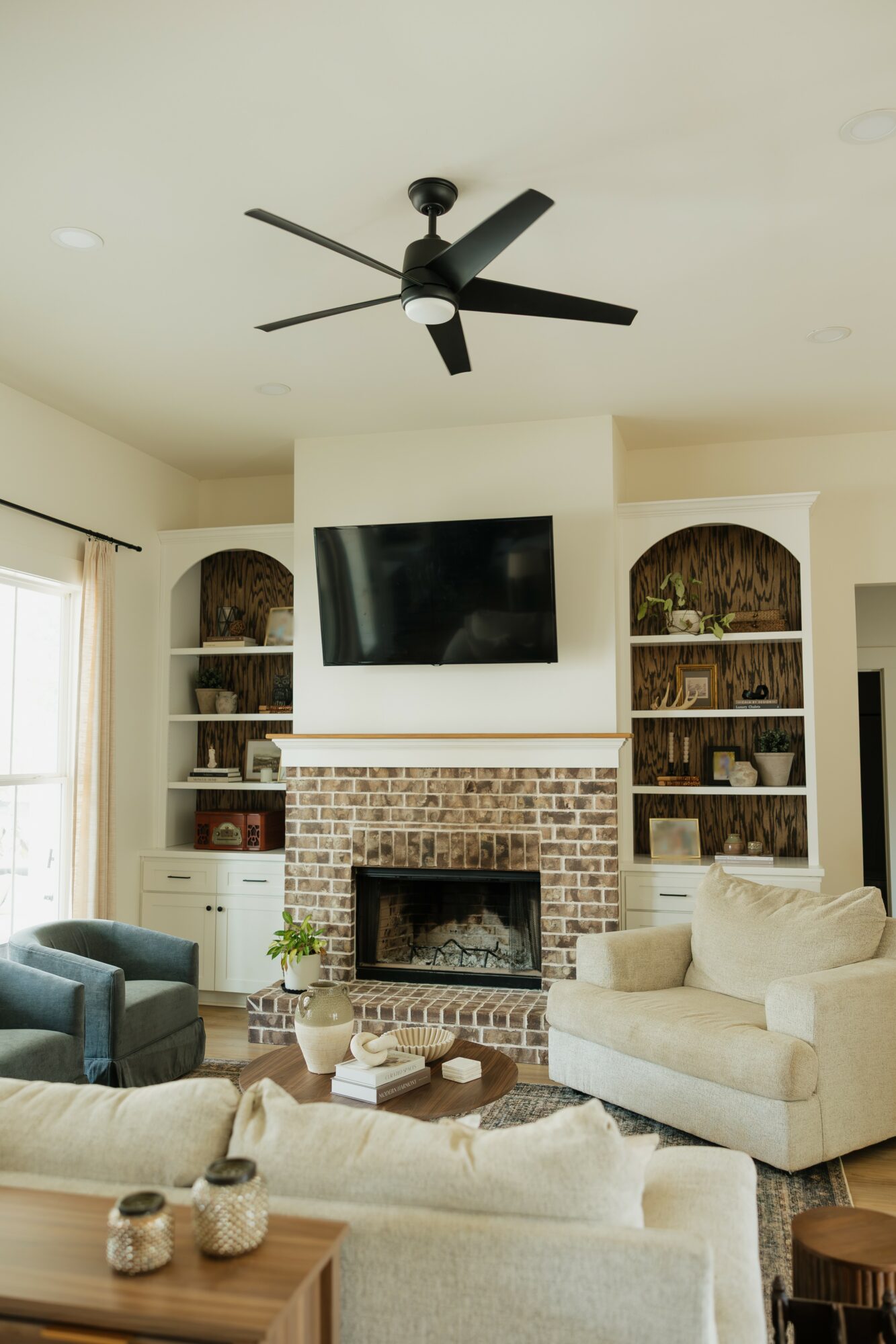 Living room with fireplace, TV, built-in shelves, ceiling fan, and seating area with sofas and armchair.