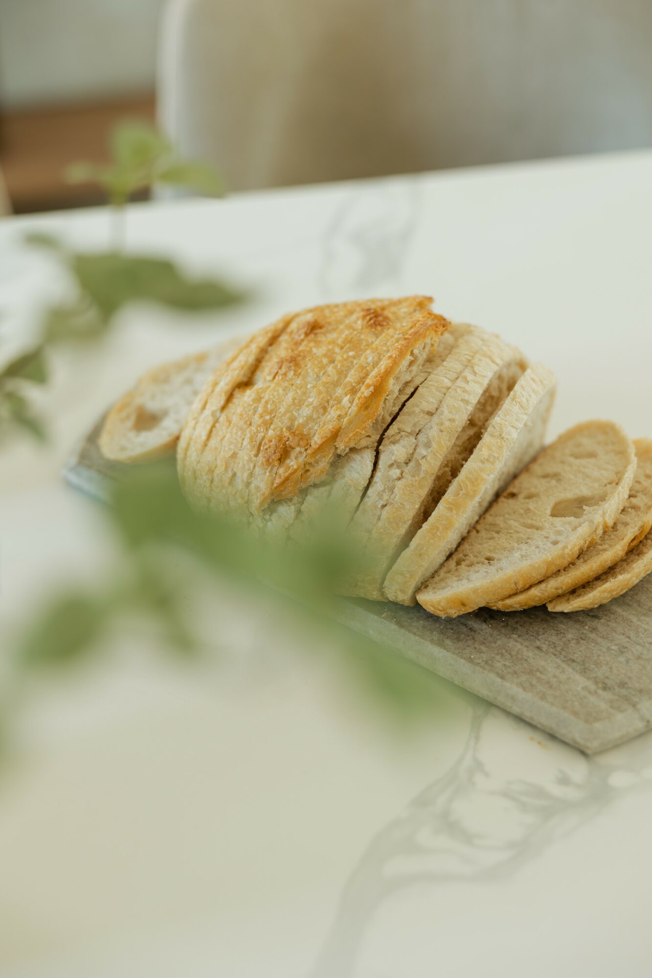 Sliced bread on a wooden cutting board with a blurred background and green leaves in the foreground.