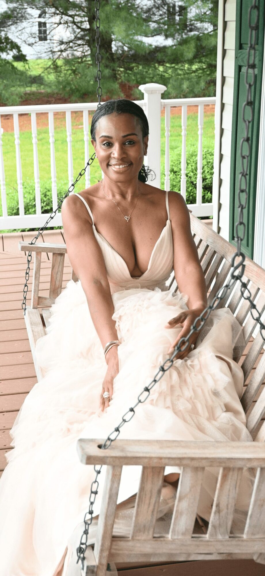 Smiling woman in a wedding dress sitting on a wooden porch swing outdoors.