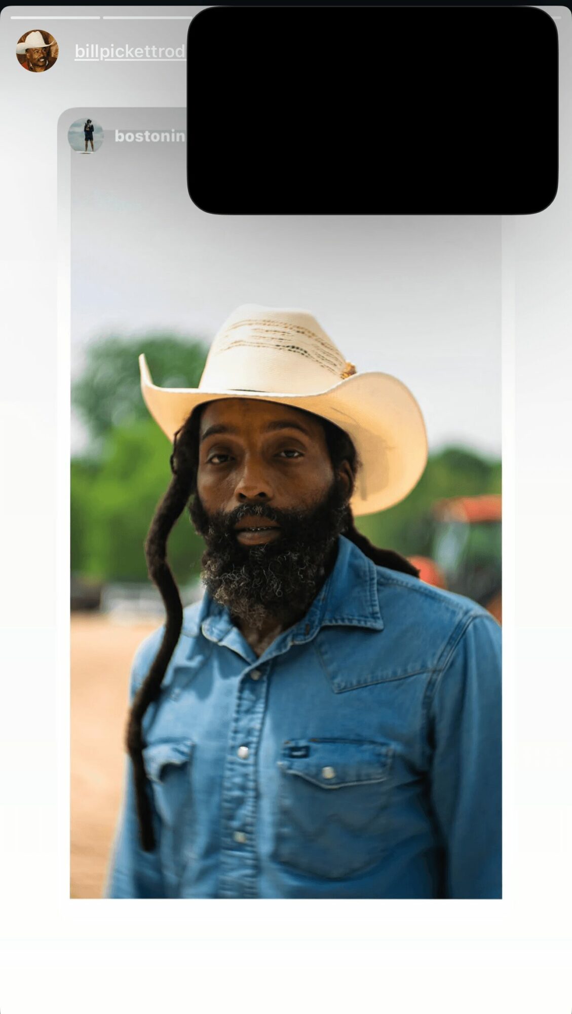 Man with a beard wearing a wide-brimmed hat and denim shirt outdoors.