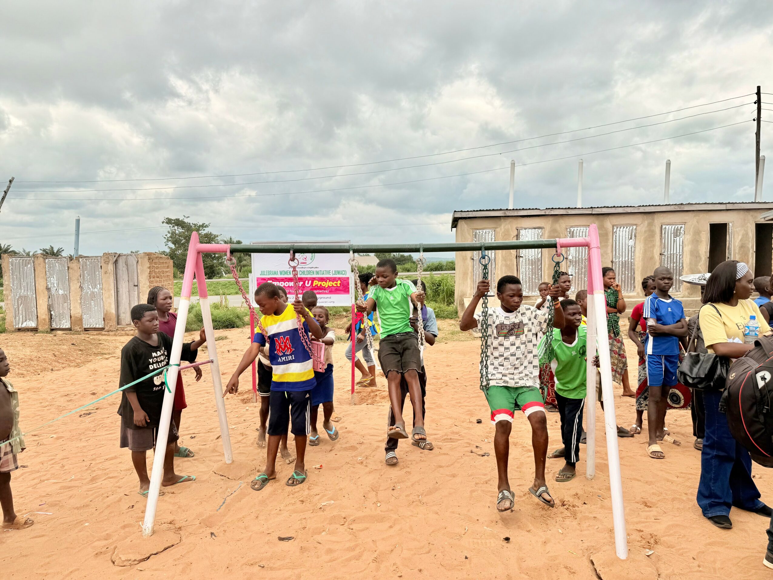Group of children playing on swings in an outdoor area with a building and cloudy sky in background.