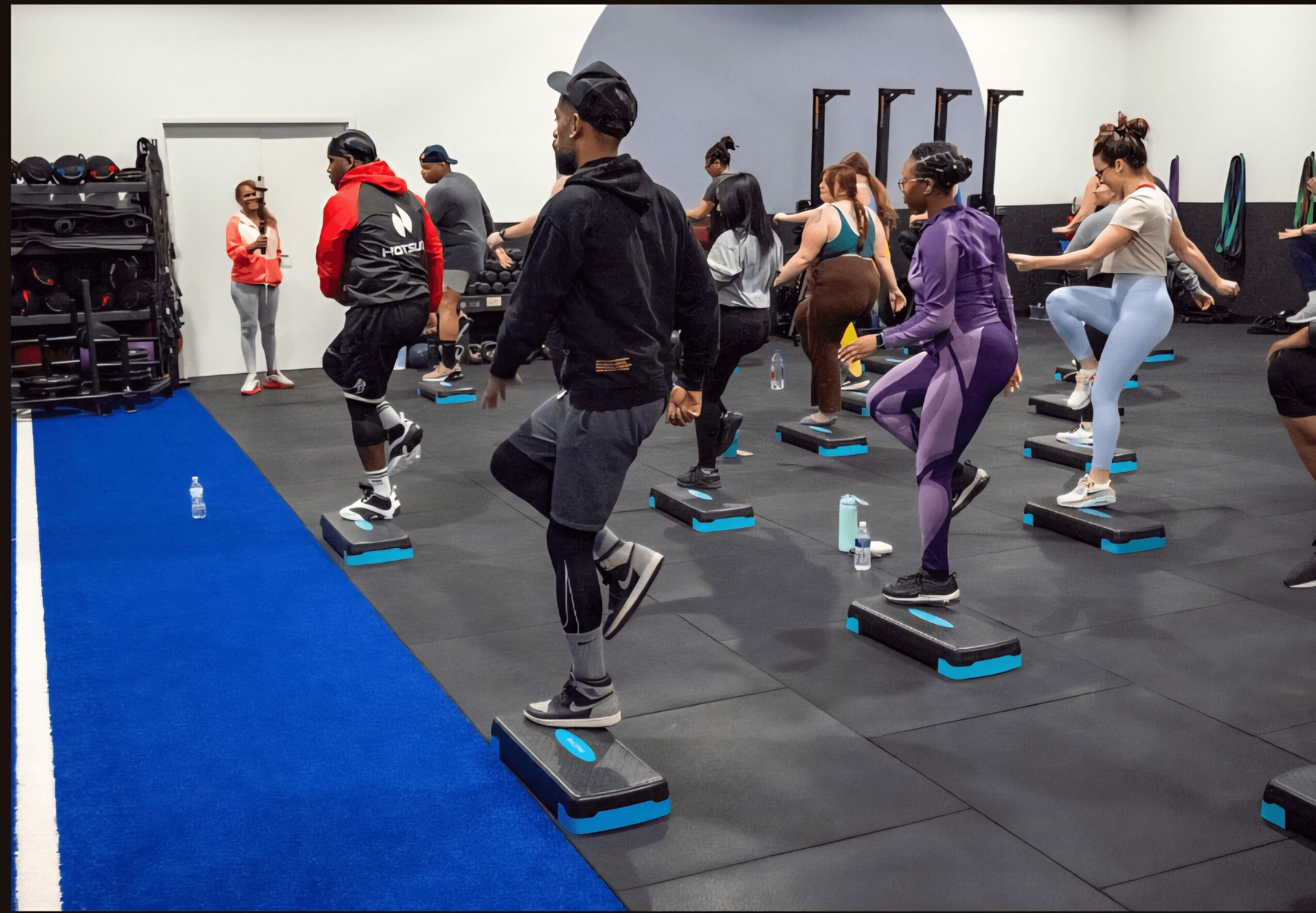 Group of people participating in a step aerobics class on individual platforms in a gym.