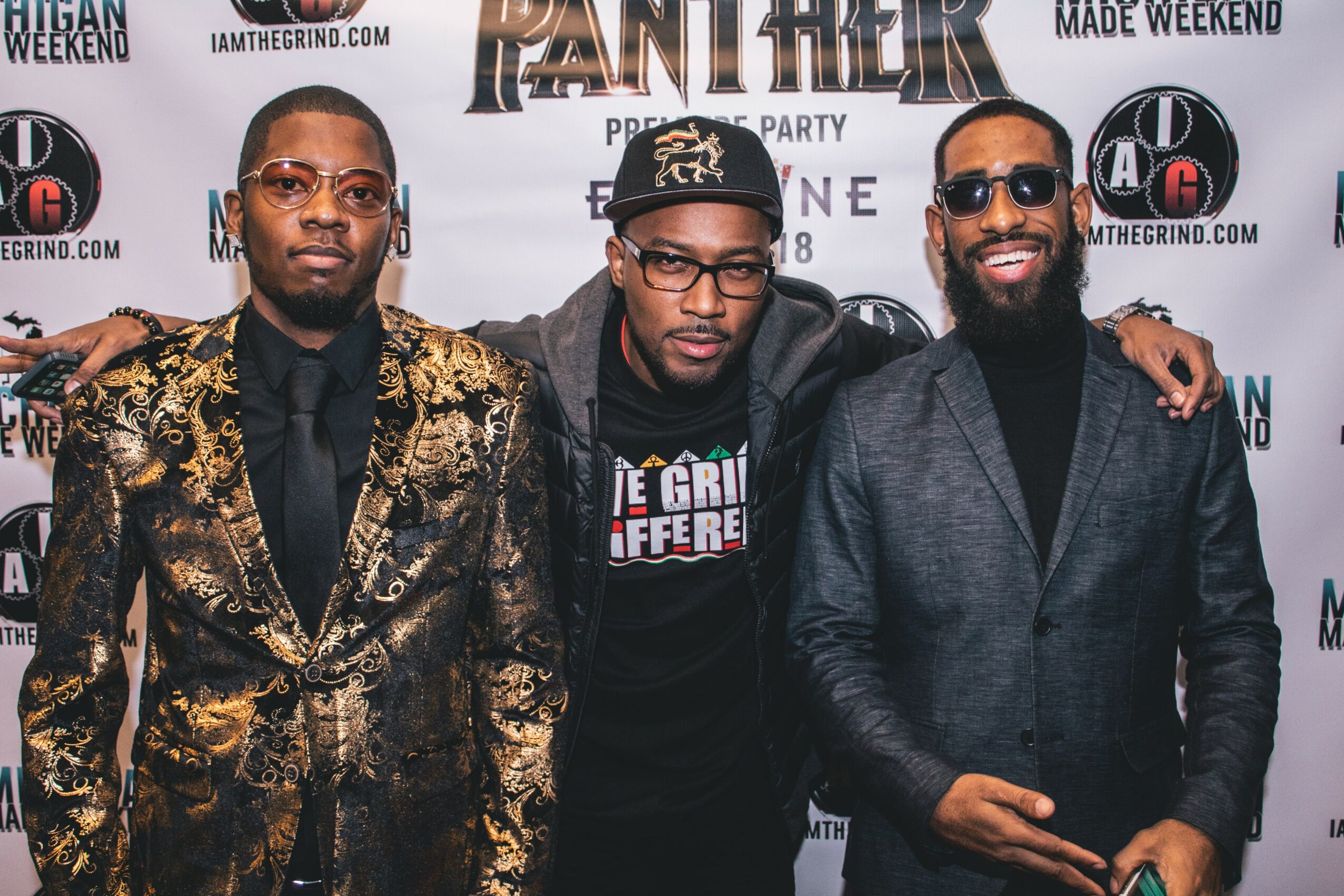 Three men standing together at a promotional event, smiling, with a backdrop featuring movie and event logos.