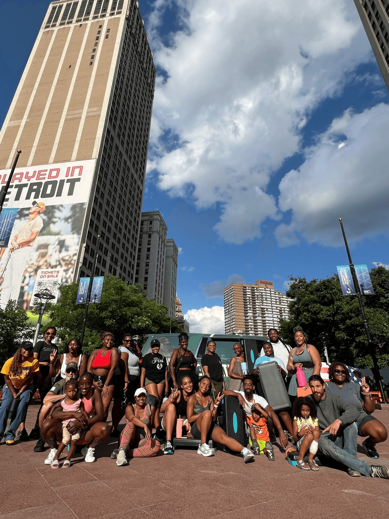 Group of people posing outdoors in an urban area with tall buildings and blue sky with clouds.