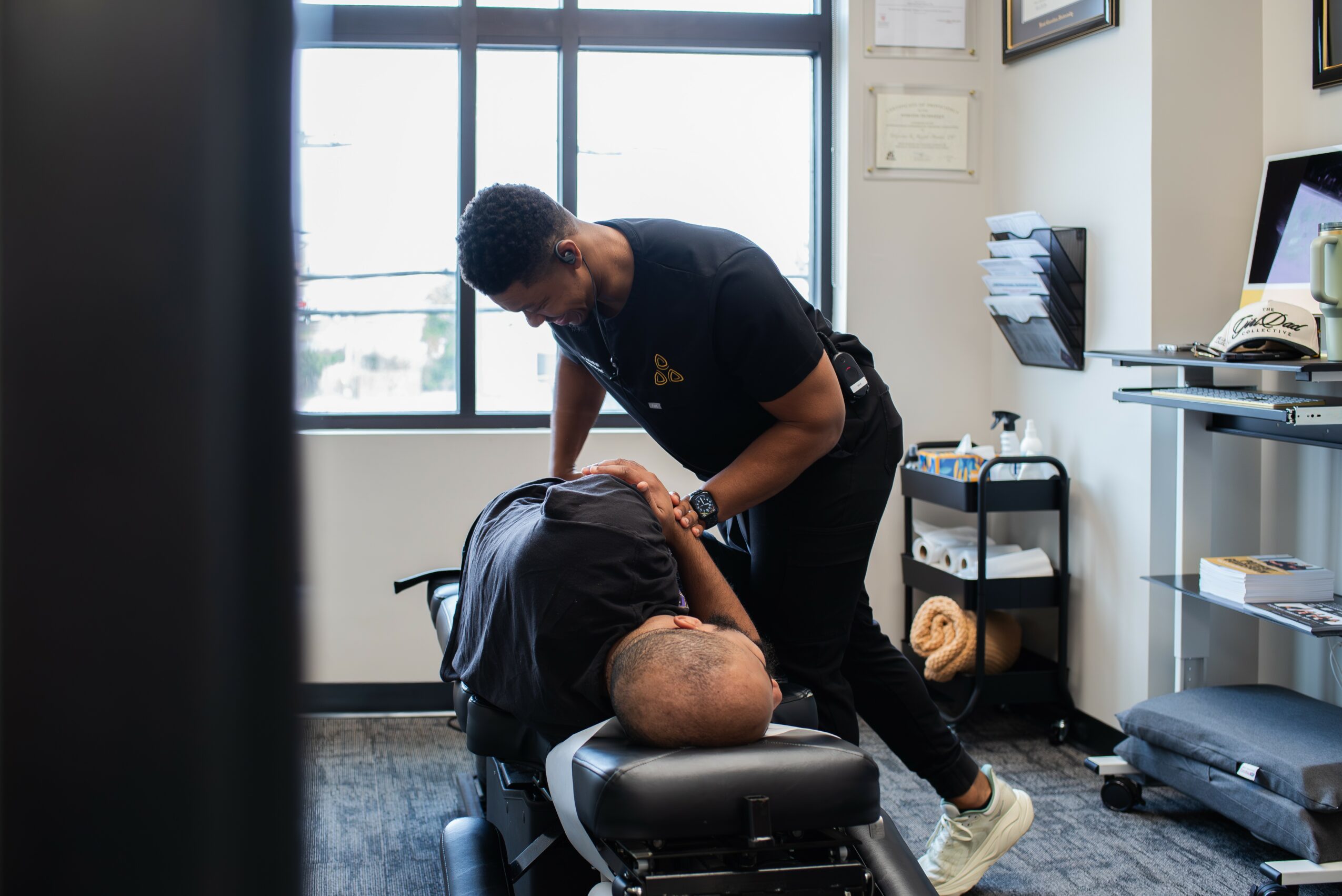 A person receiving a head massage from a massage therapist in a room with large windows and office furniture.