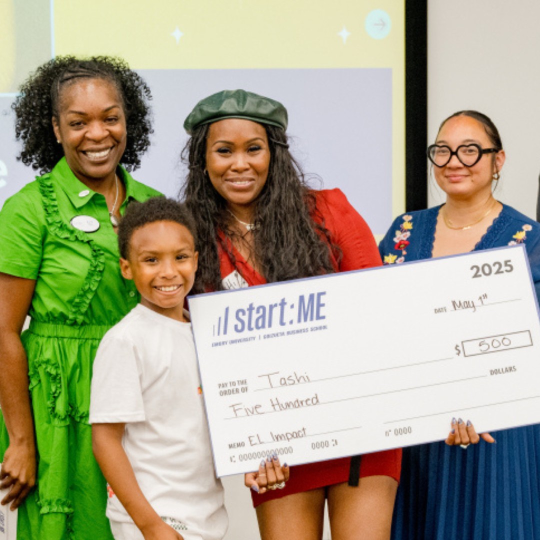 Four women and a girl holding a large check, smiling, in a room with a screen in the background.