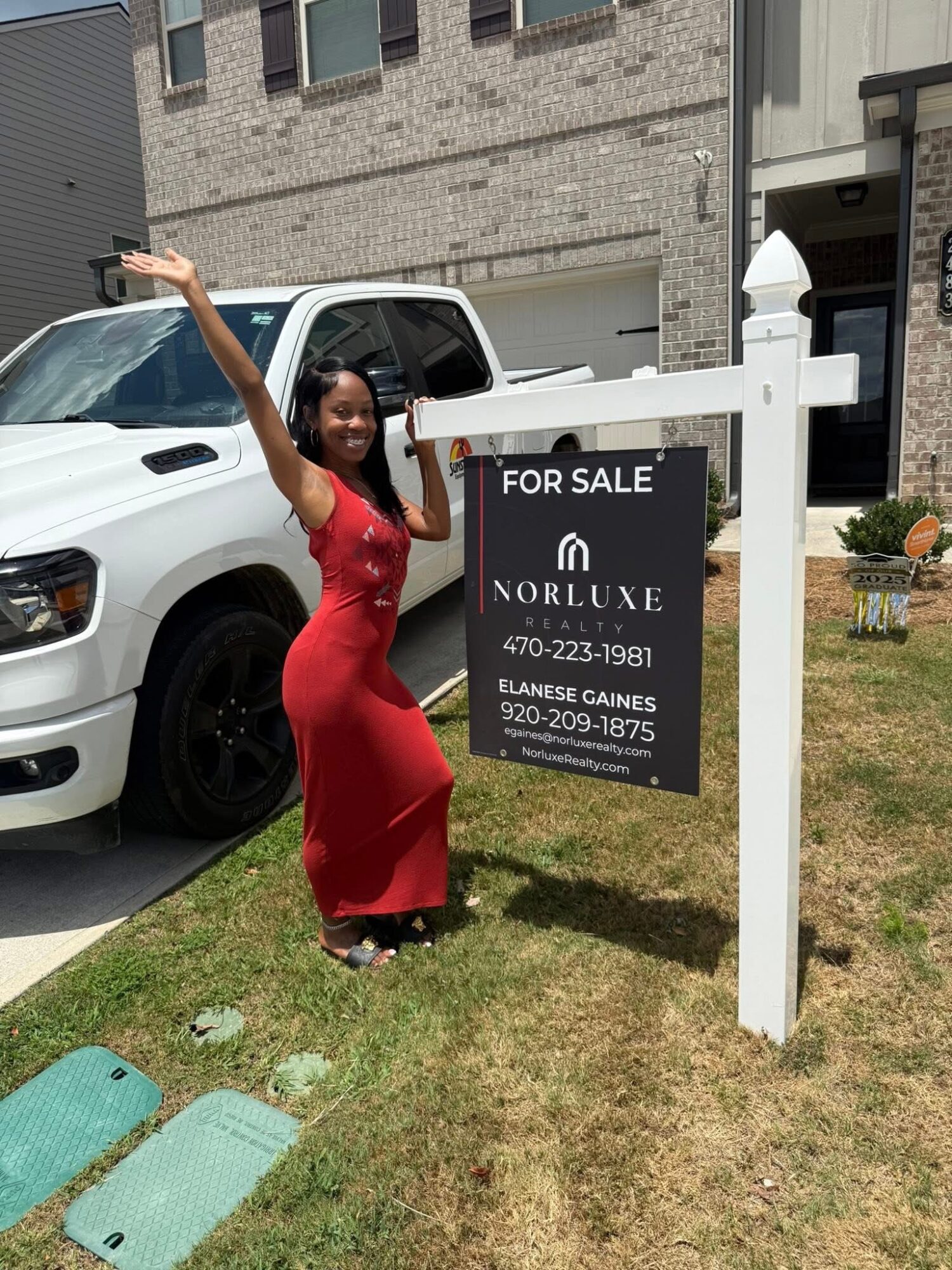 Woman in red dress taking a selfie next to a for sale sign outside a building.