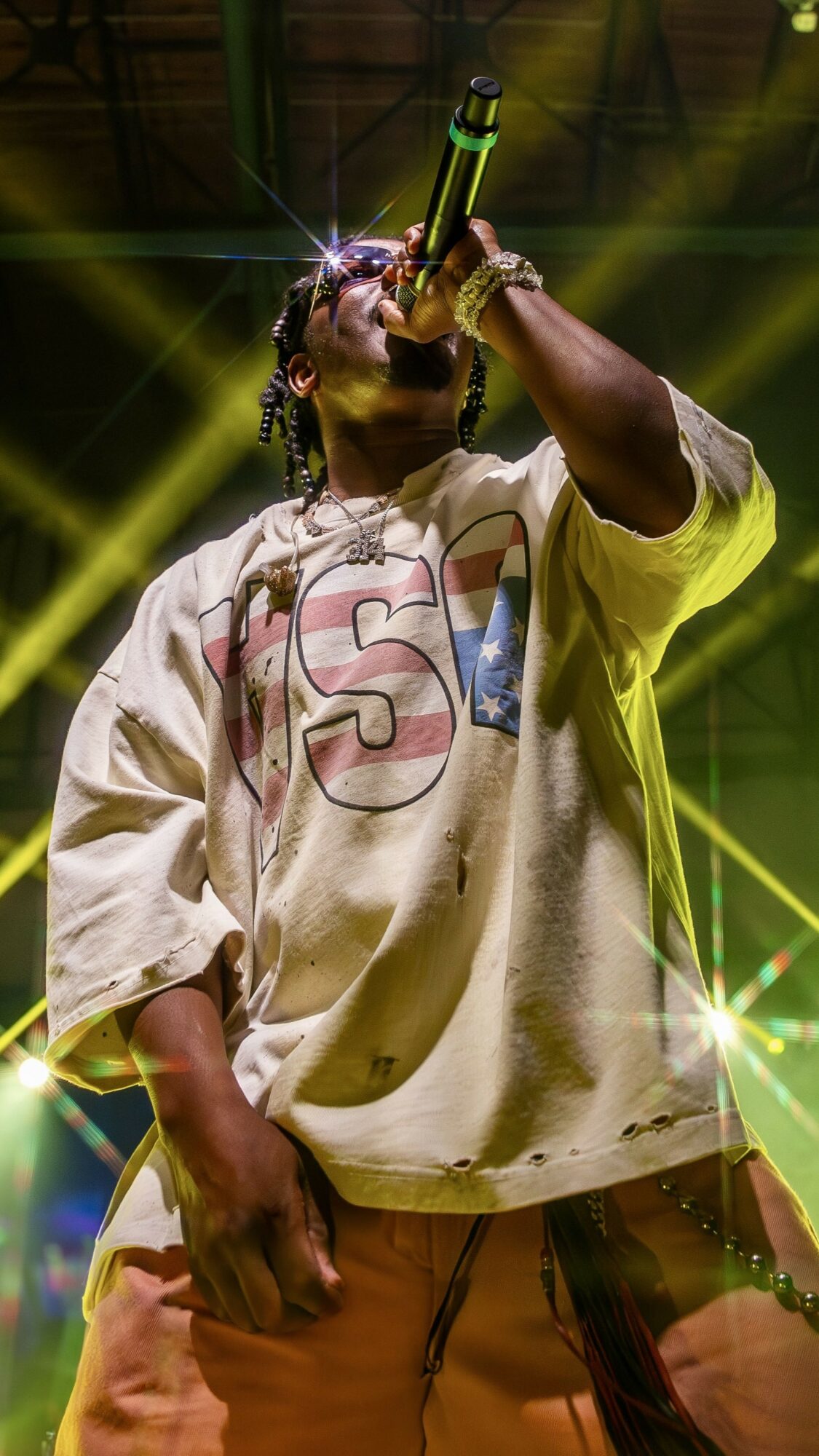 Performer singing into microphone on stage with yellow lighting and stage effects.