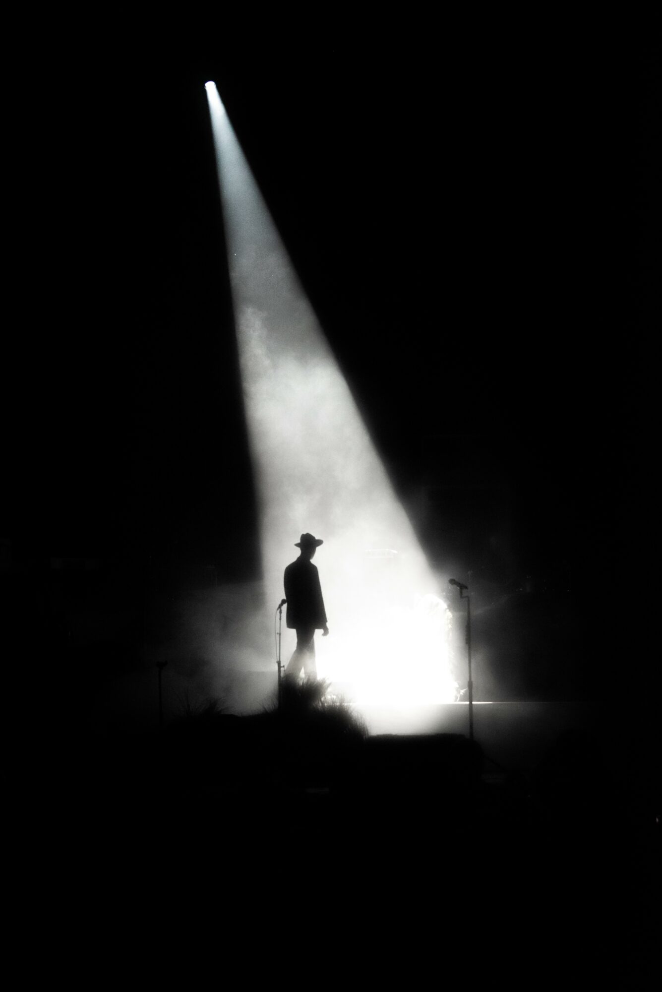 Person standing on stage illuminated by a spotlight with dark surroundings.