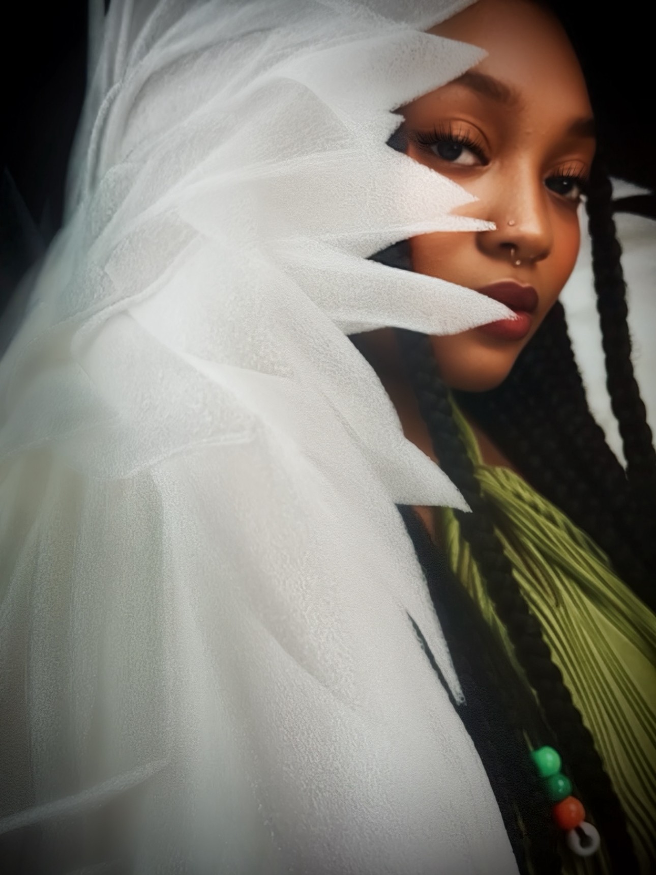 Close-up of a woman with dark braided hair, wearing a white layered head covering and a green garment with beads.