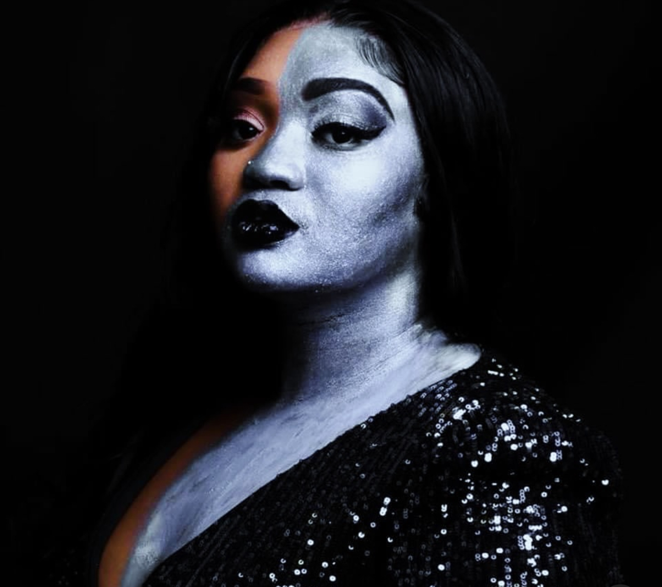 Woman with makeup and dark hair, wearing a sequined top, against a dark background.