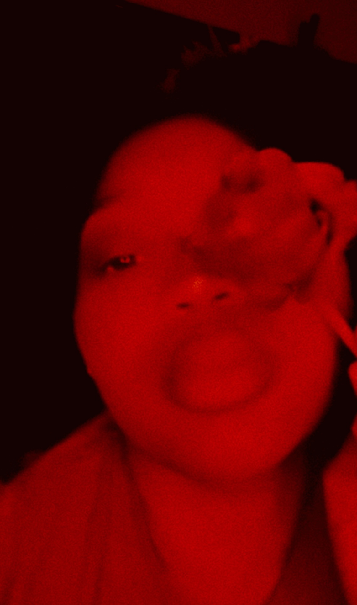 Person with face partially obscured by red lighting, lips slightly parted, dark background.