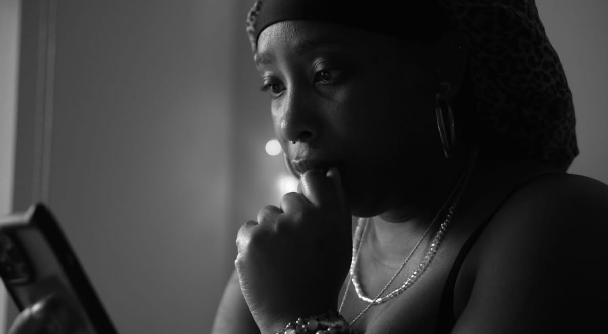 Woman looking at a phone with hand near mouth, indoors, dim lighting, wearing jewelry and head covering.