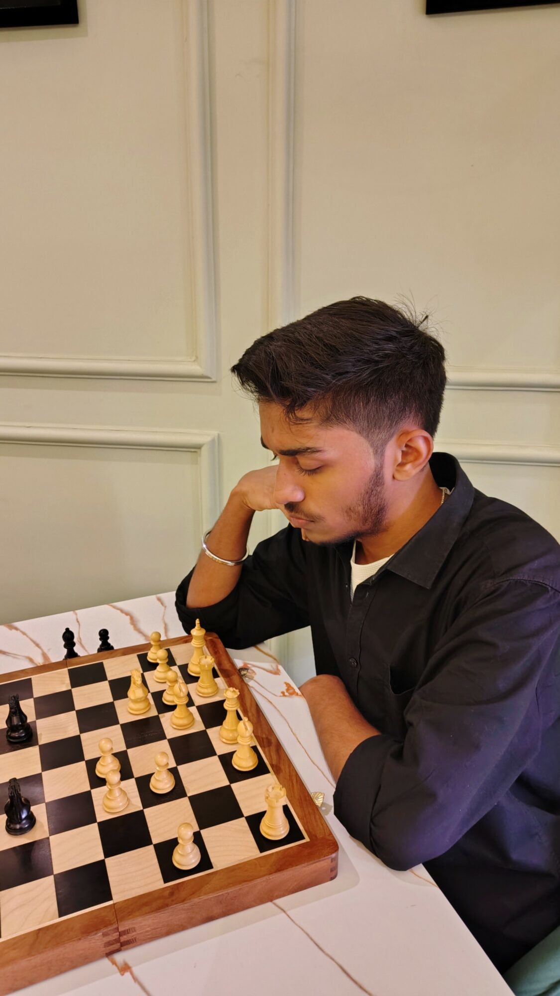 Young man playing chess, resting his head on his hand, focused on the game.