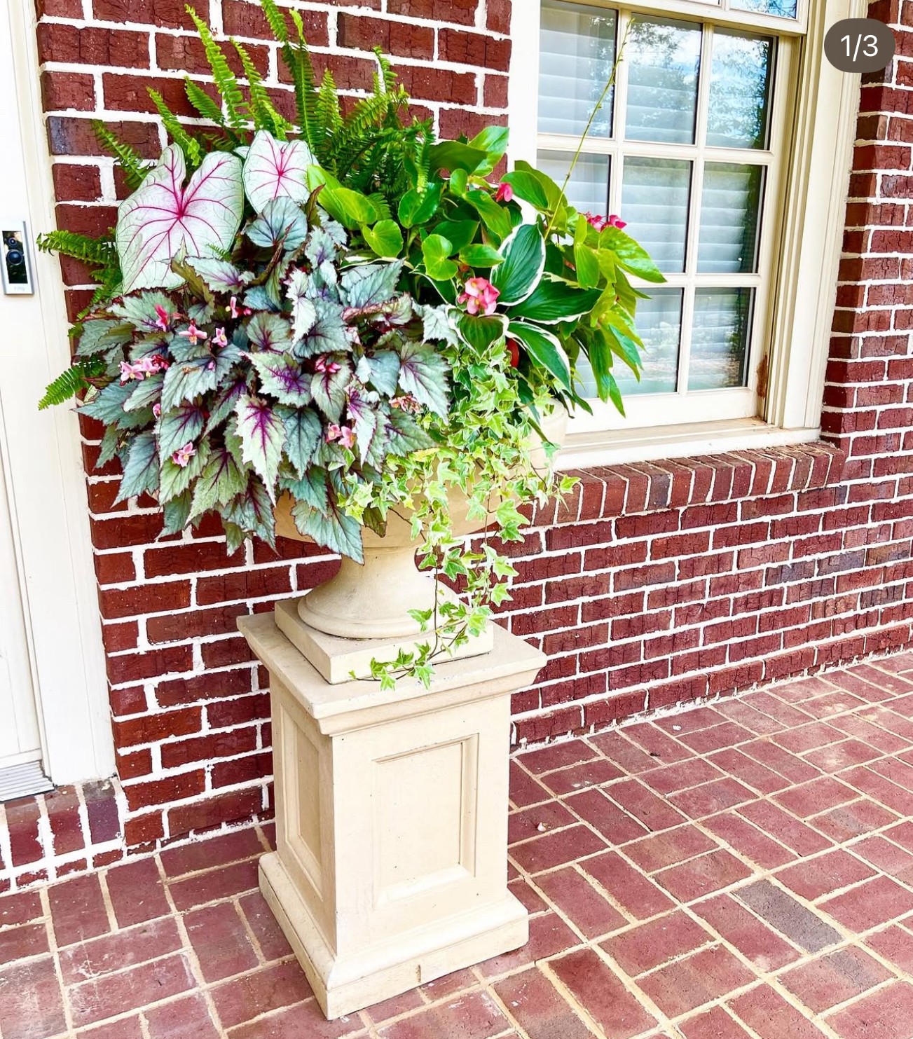 Flower arrangement in a white planter on a brick porch with a window in the background.