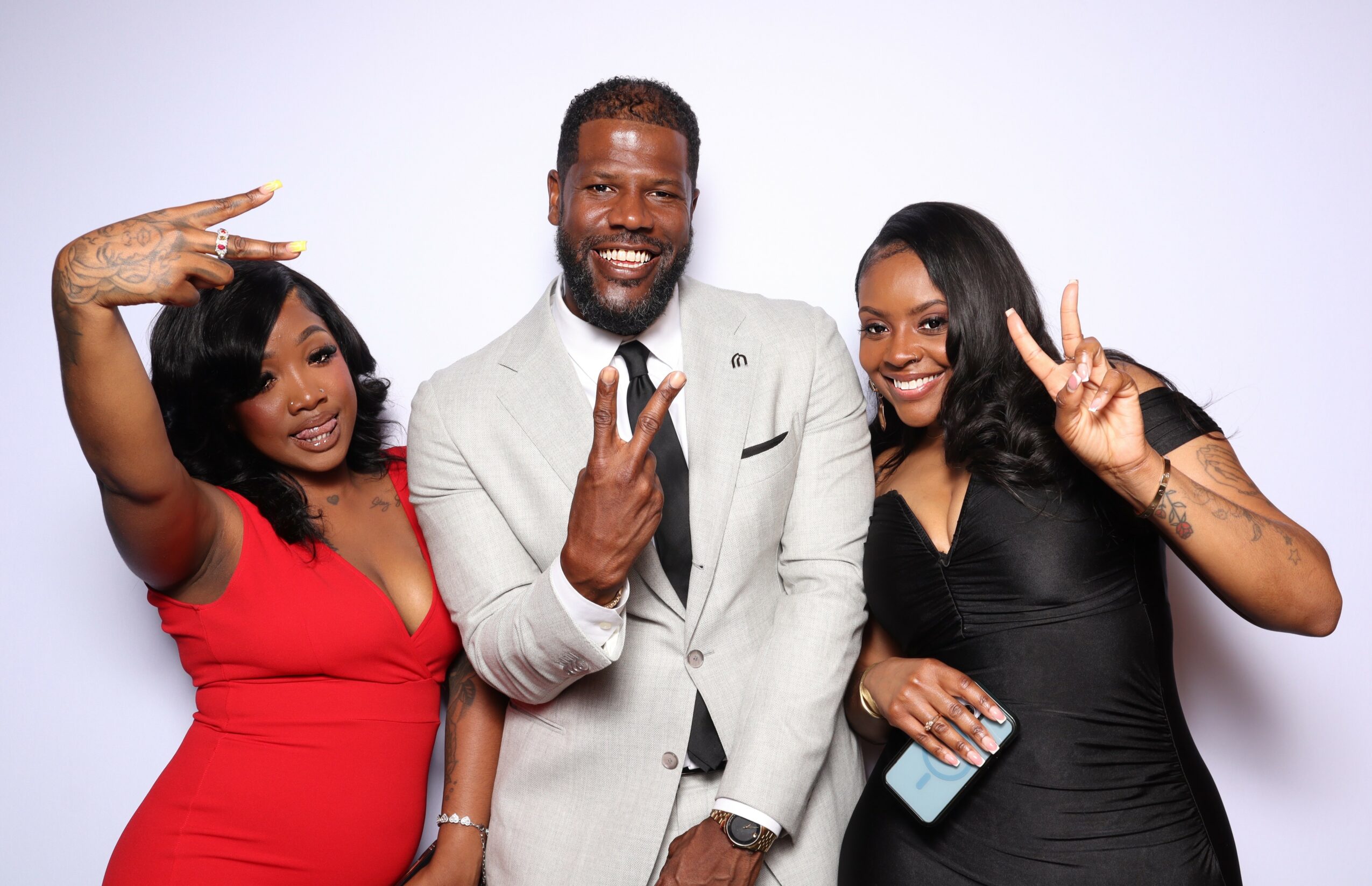 Three people smiling and making peace signs, standing against a plain white background.