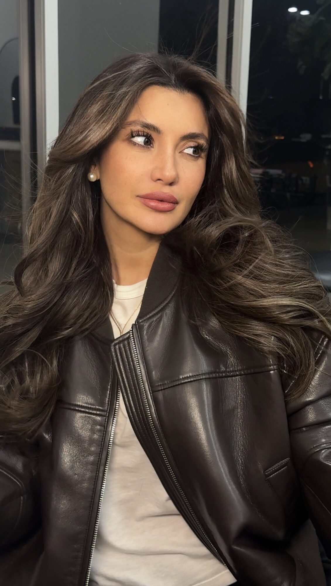 Woman with long wavy hair wearing a leather jacket indoors at night.