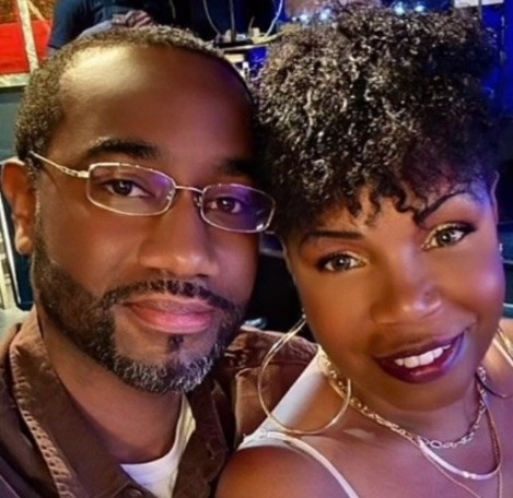 Close-up of a man and woman smiling, with the man wearing glasses and the woman with curly hair and hoop earrings.