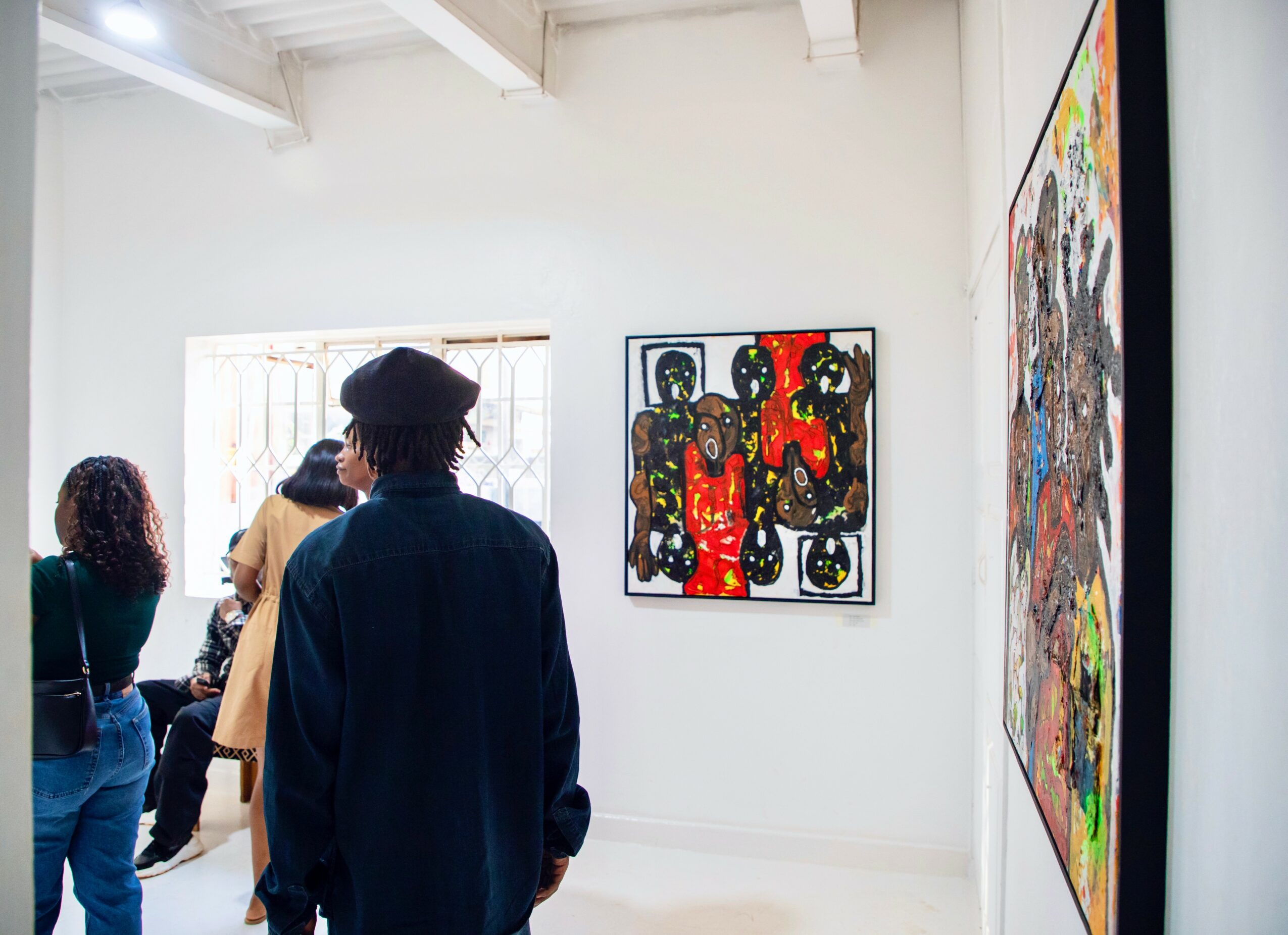 People viewing colorful abstract paintings in an art gallery with white walls and natural light.