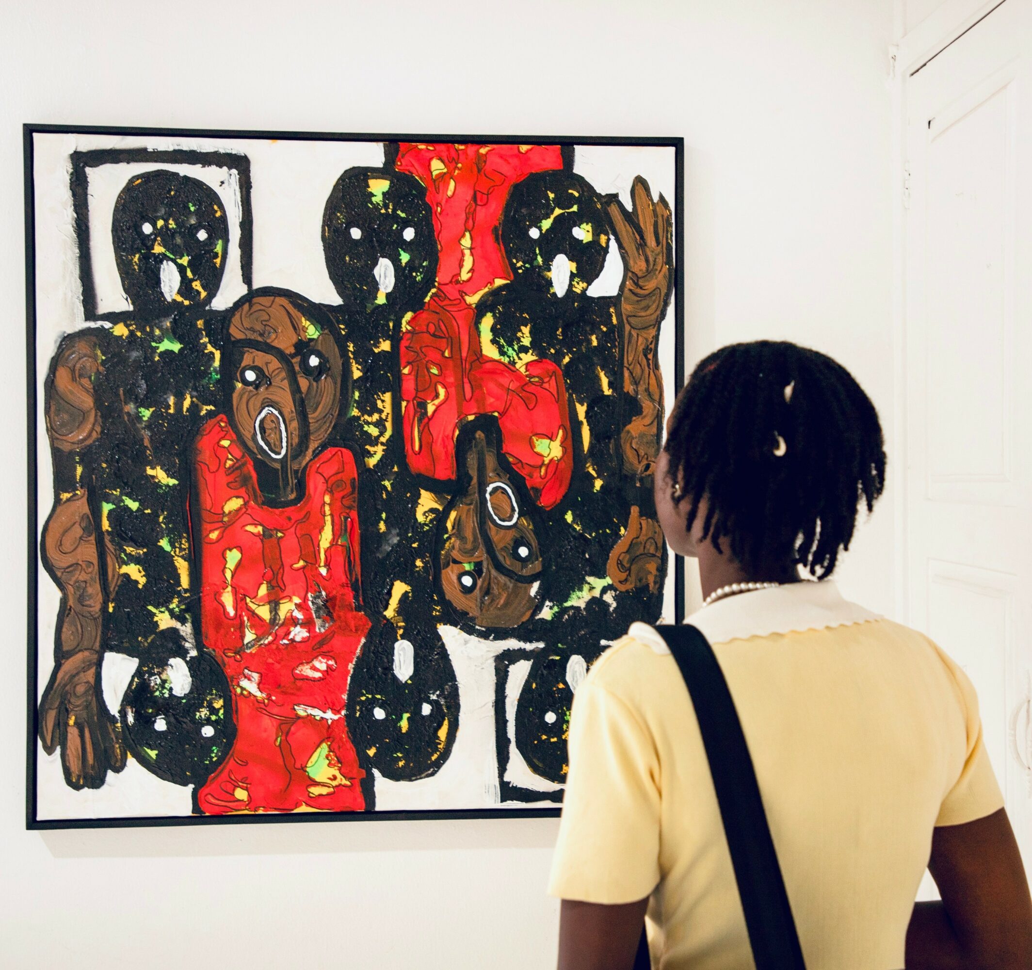 Person with short hair and yellow shirt viewing colorful abstract artwork in gallery.