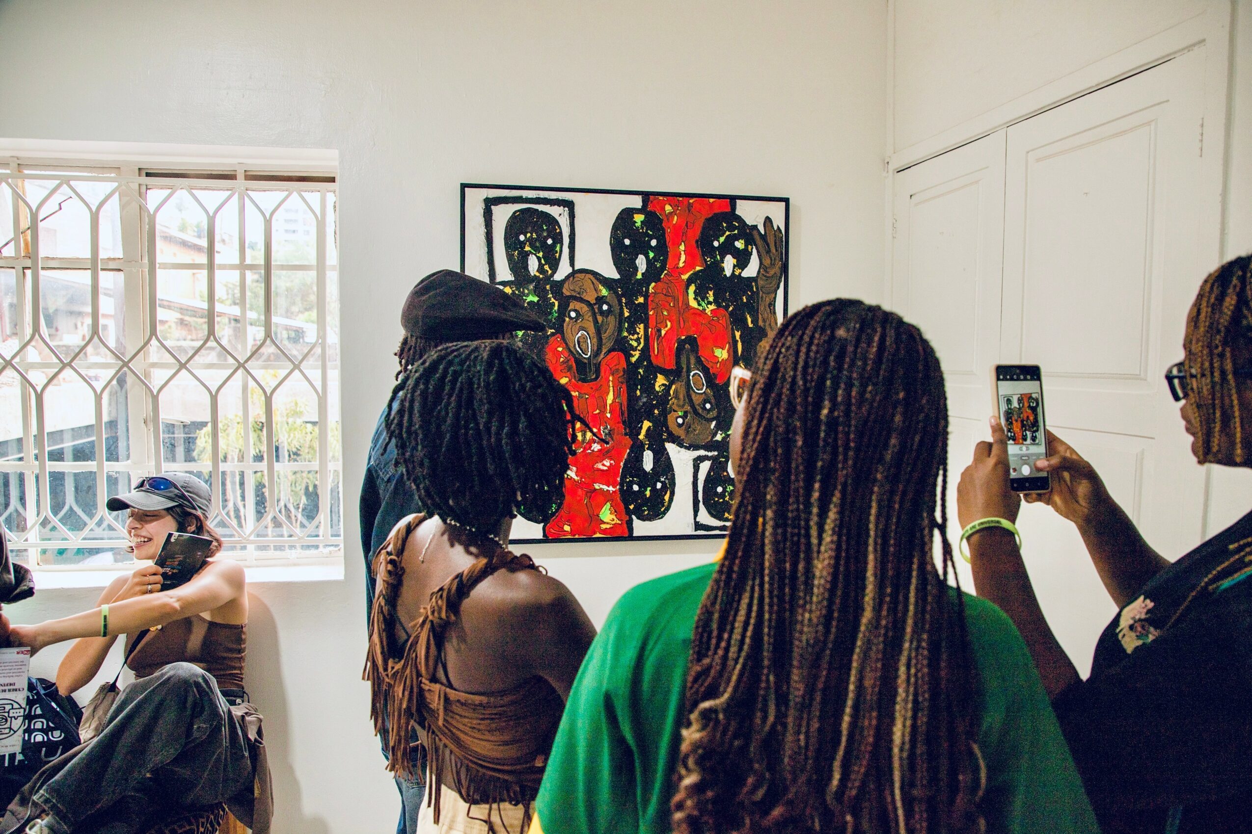 Group of people in an art gallery viewing colorful paintings on the wall, some taking photos.