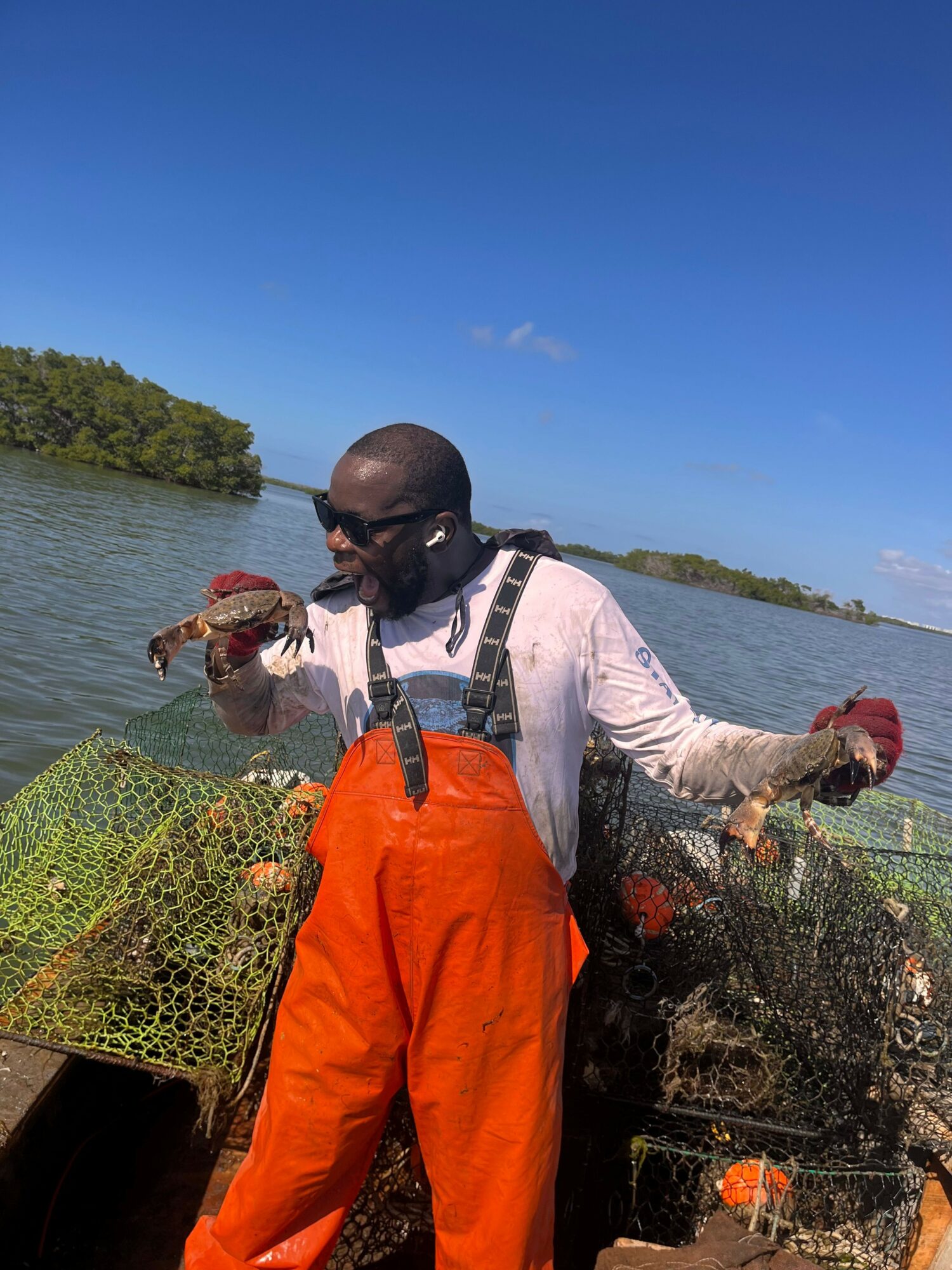 Person holding a crab on a boat with water and trees in the background.
