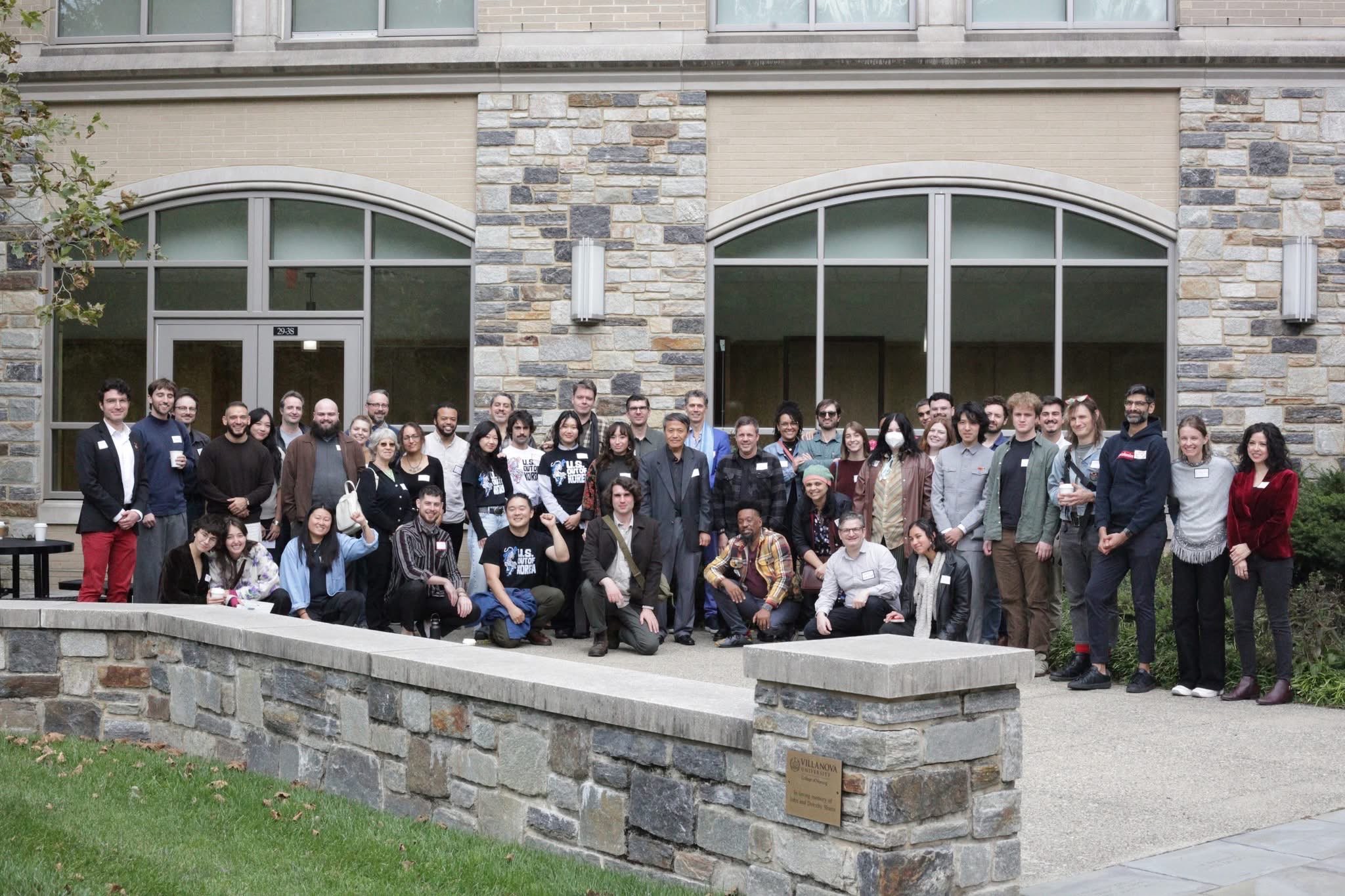 Large group of people standing outside a building with stone and glass facade, posing for a photo.