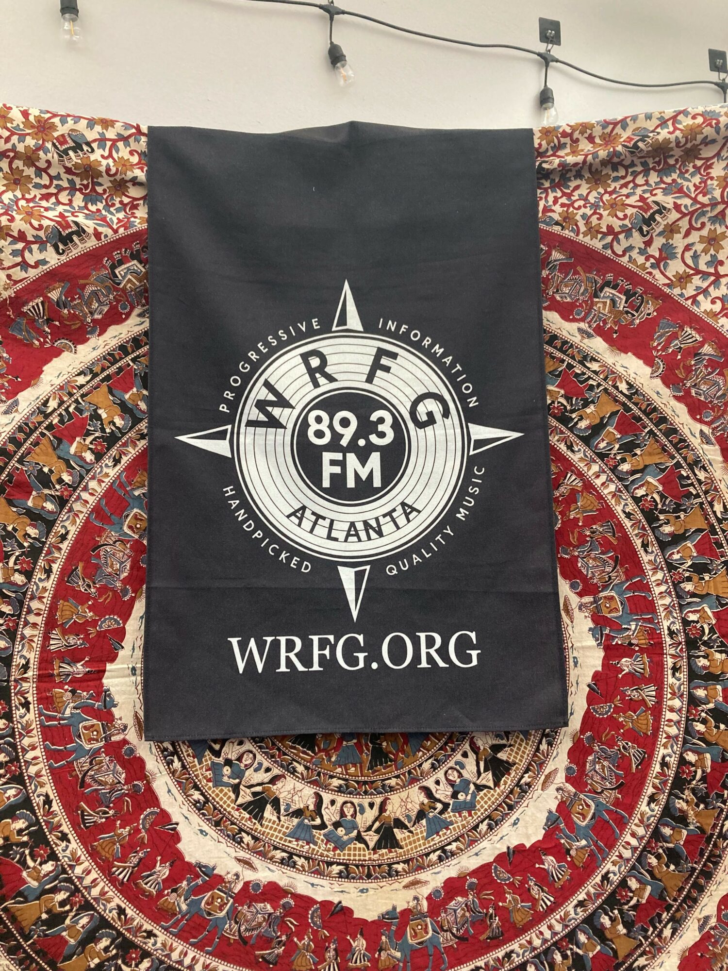 Black fabric banner with WREG 89.3 FM Atlanta logo and website, hanging in front of a patterned rug.
