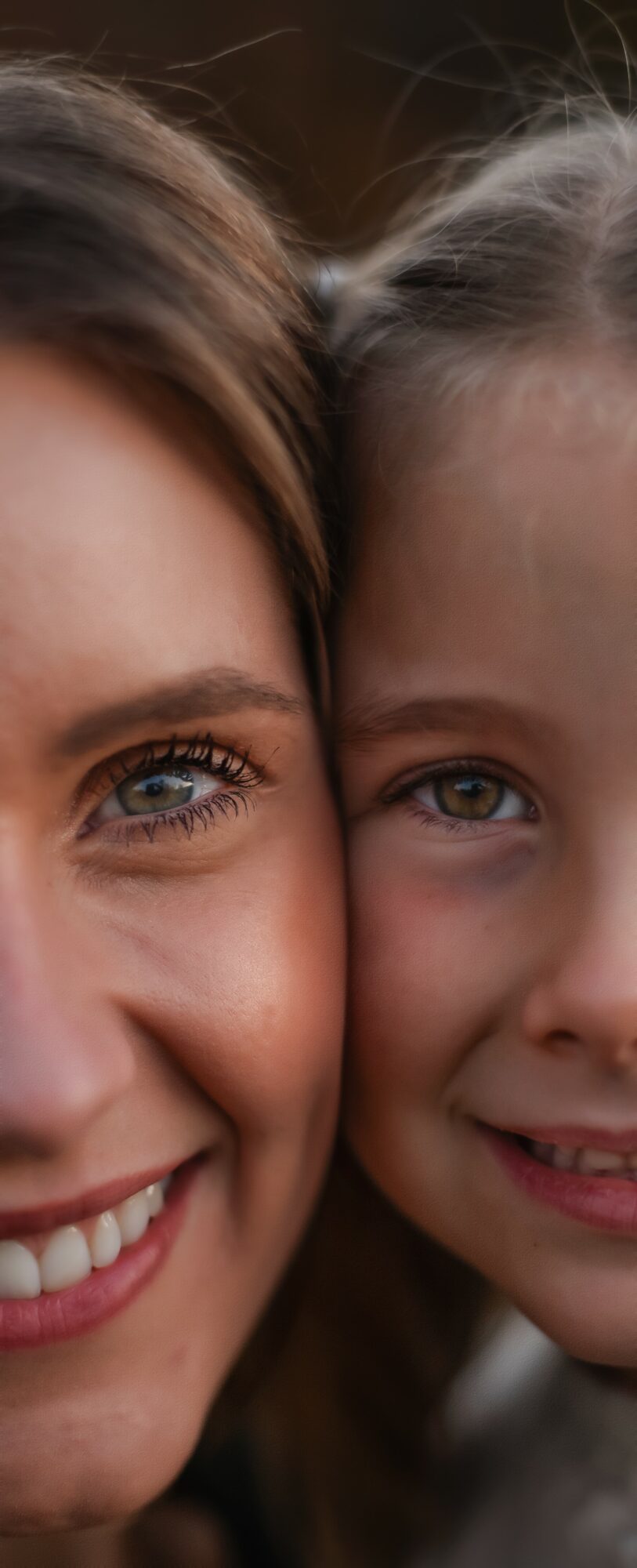 Close-up of a woman and a girl smiling, showing their faces and eyes.