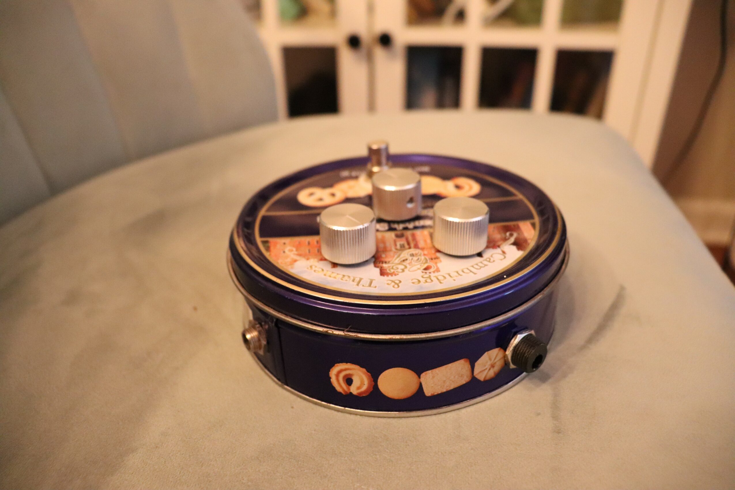 Round vintage music box with a dark blue body and decorative elements on top, placed on a light-colored surface.