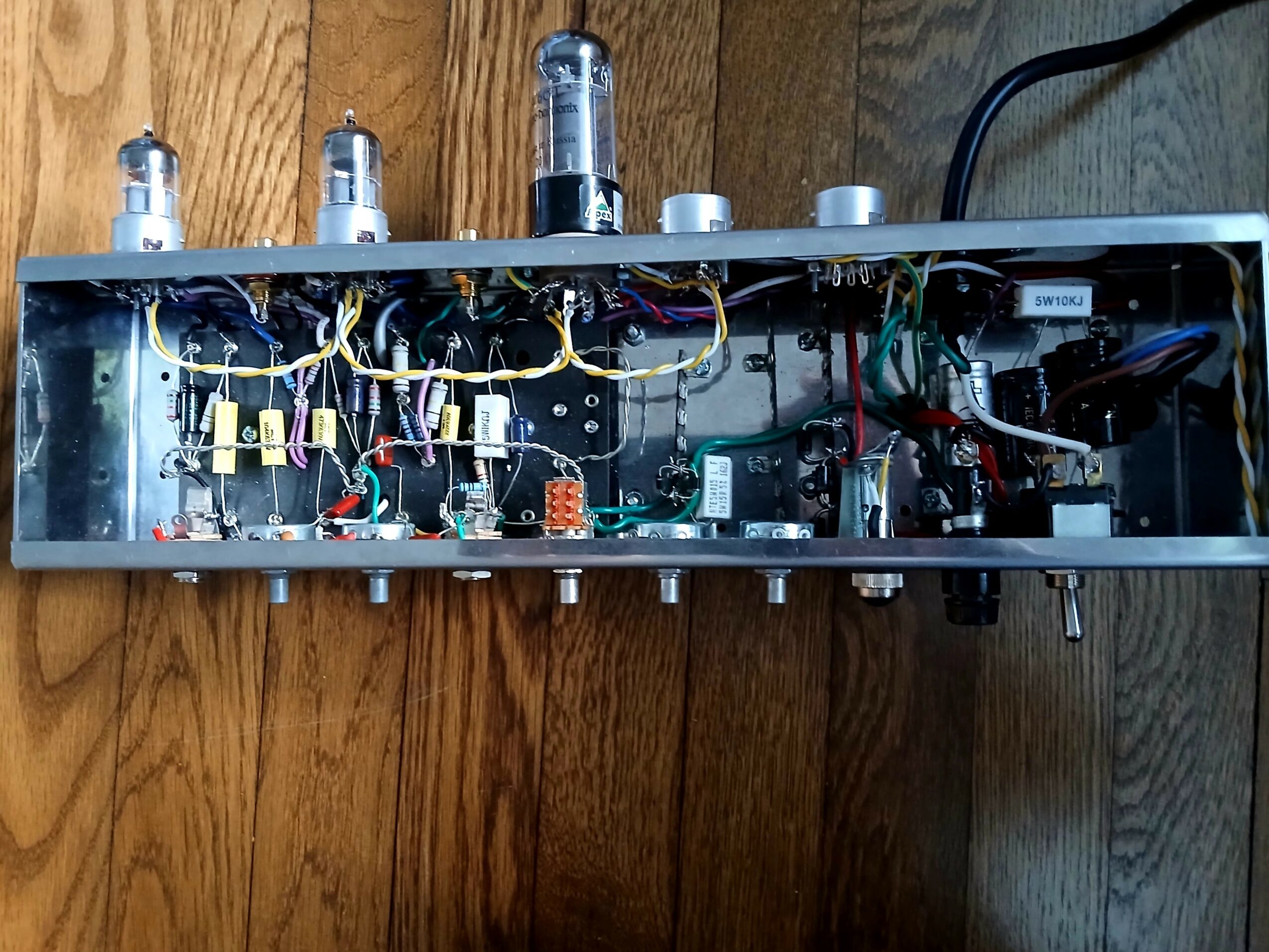 Open electronic device with vacuum tubes, wires, and circuit components inside a metal case on a wooden surface.