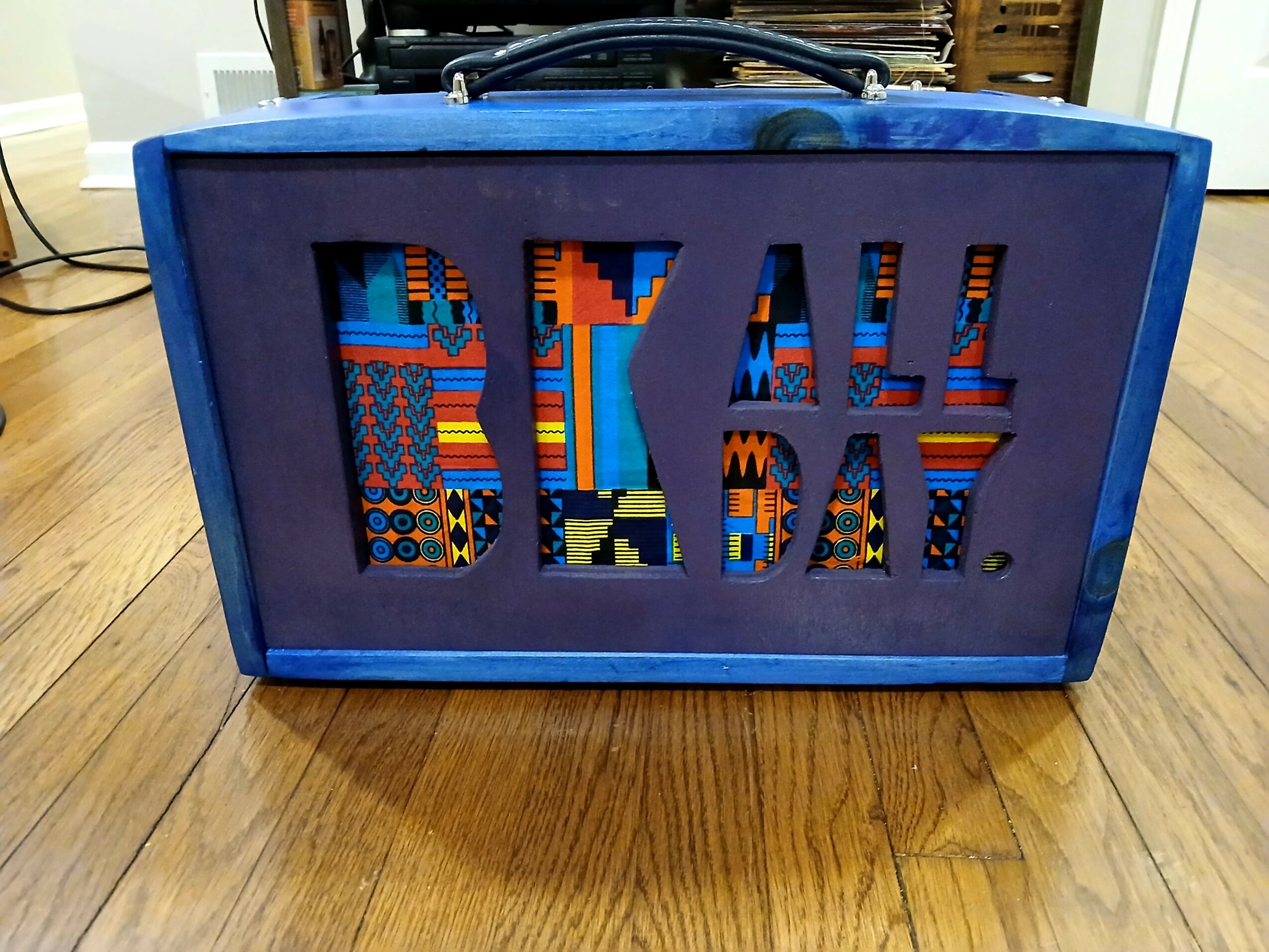 Blue box with cut-out letters spelling 'BEACH' filled with colorful patterns, on a wooden floor.