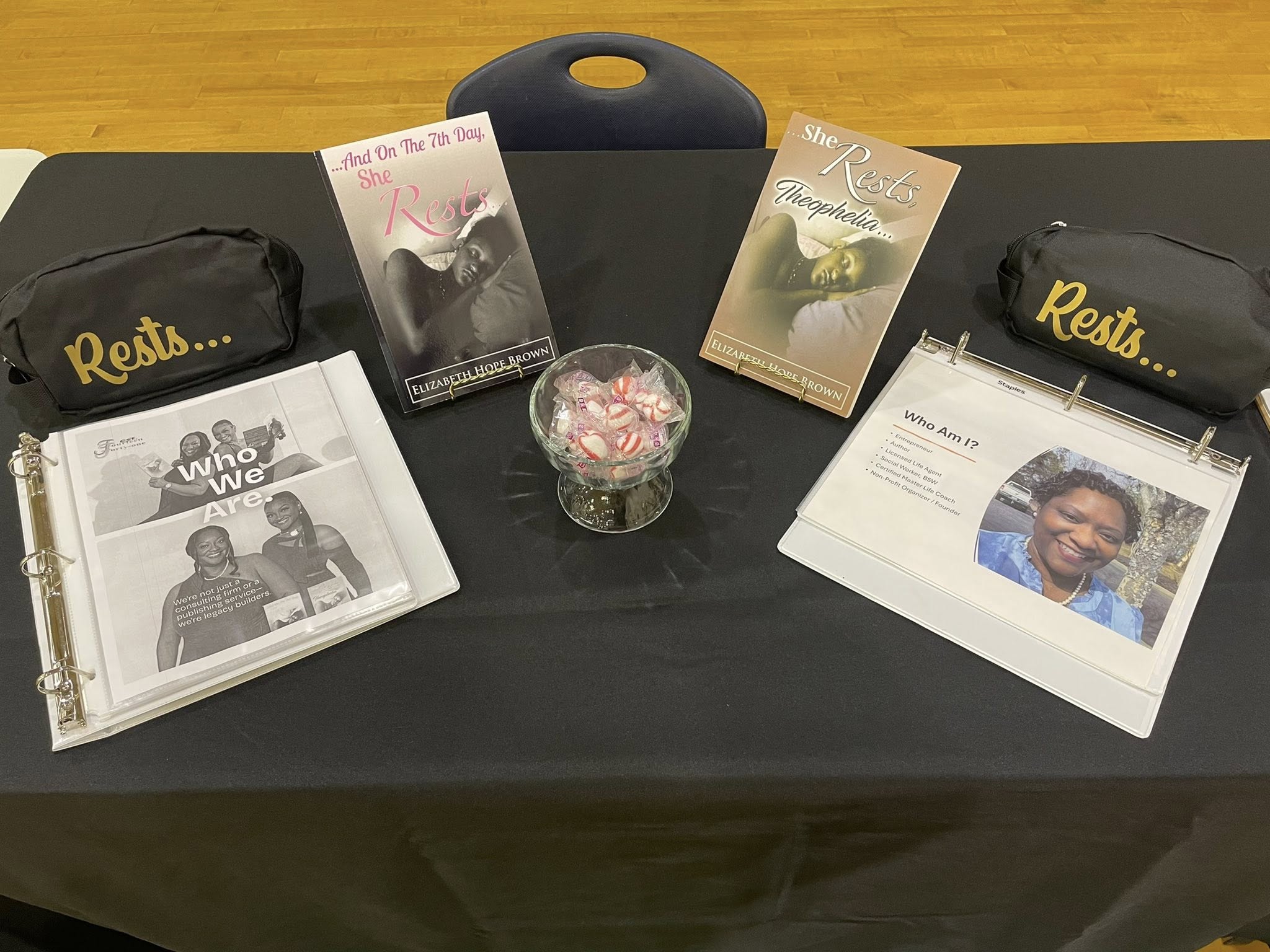 Table with books, a glass bowl, and two black pouches labeled 'Rest...'. Items include a photo album, pamphlets, and a framed picture of a person.