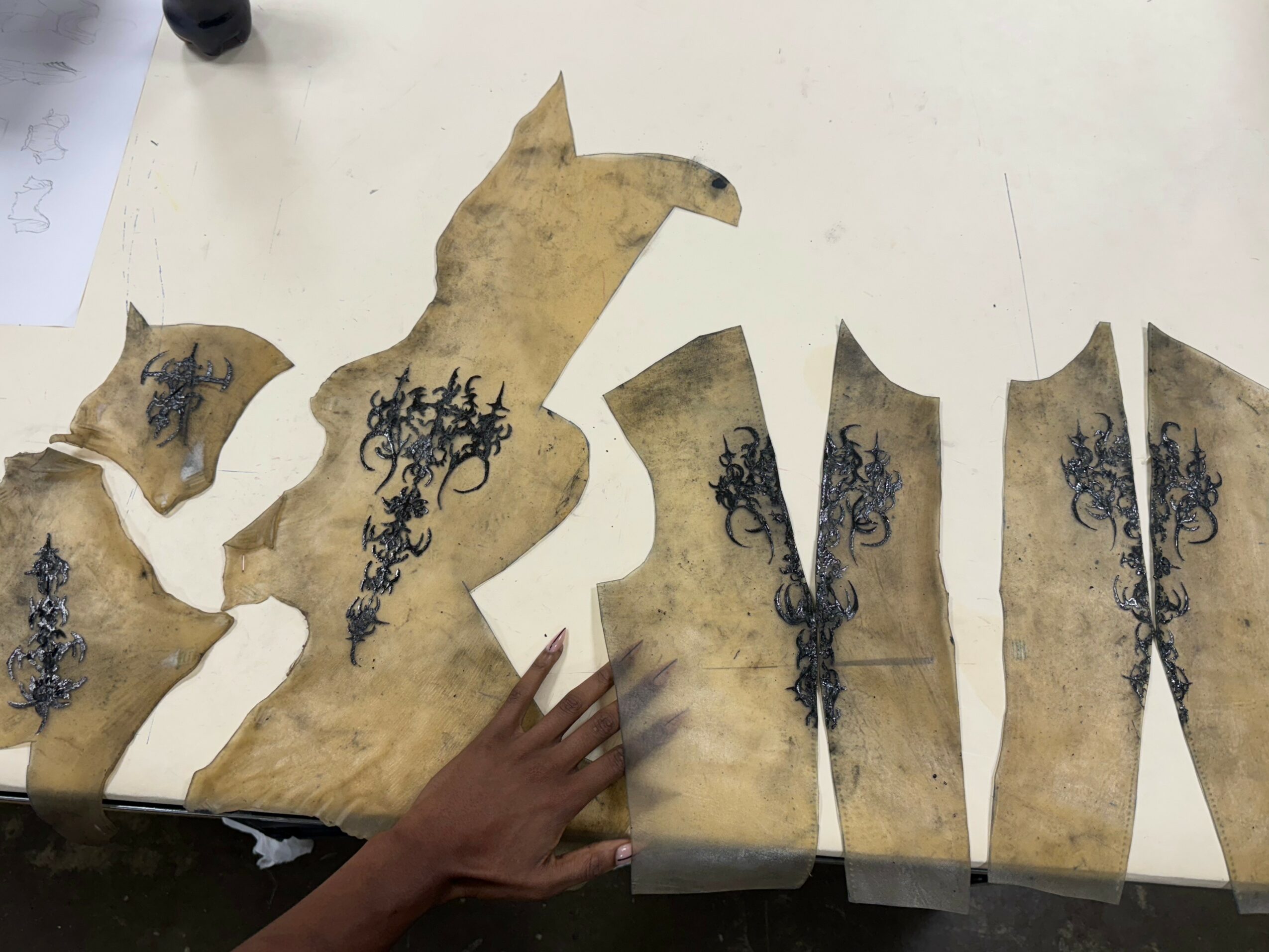 Pieces of aged parchment with black ink illustrations, some shaped like animals, on a white surface. A hand touches one piece.