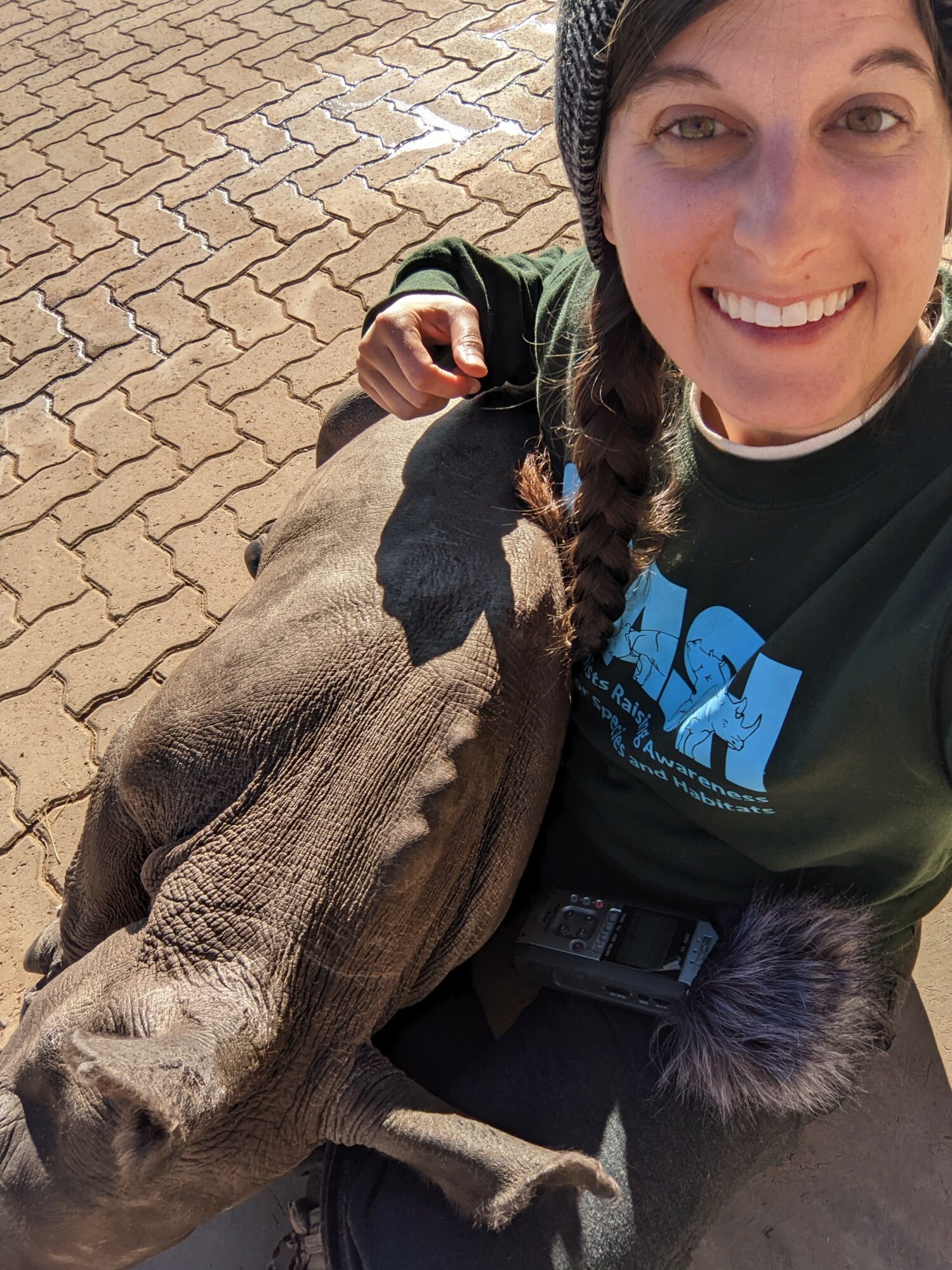 Woman smiling with a baby elephant outdoors on a paved surface.