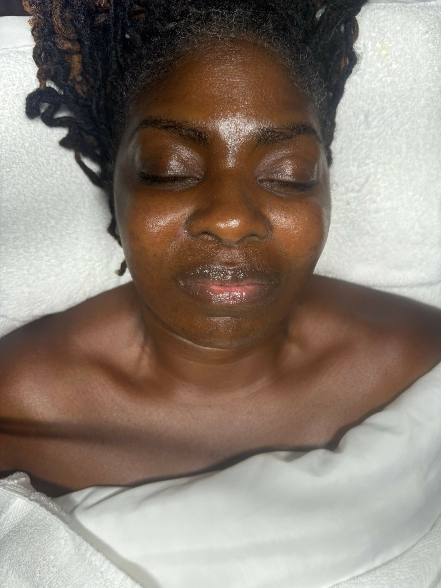 Close-up of a woman with closed eyes and dark hair lying on a white surface.