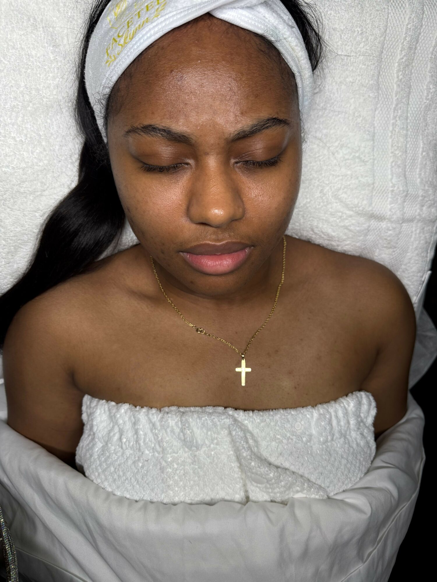 Young woman with closed eyes, wearing a headband and a cross necklace, lying on a pillow.