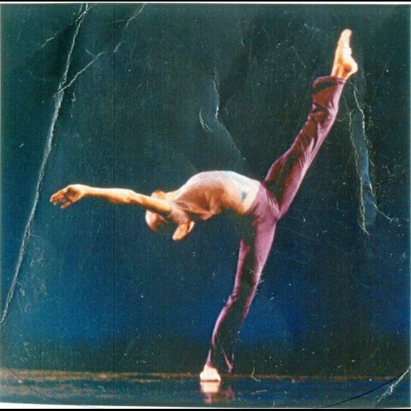 Person performing a handstand with one leg extended upward and the other bent, on a dark stage.