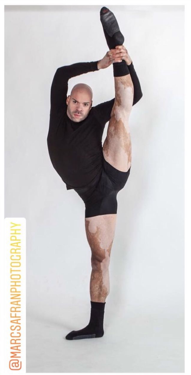 Person performing a standing high leg stretch, holding foot with hand, against a plain white background.