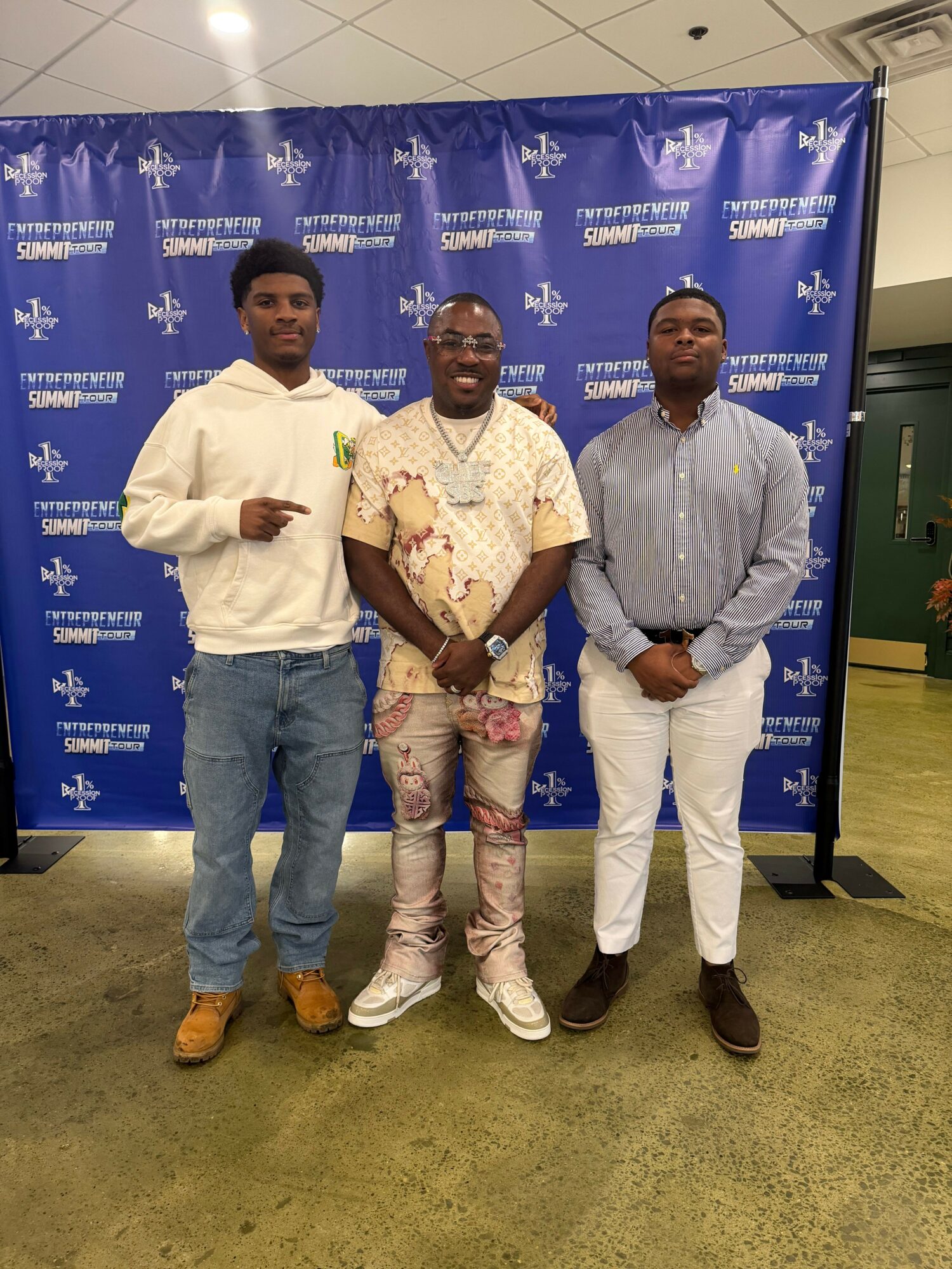 Three men standing in front of a blue backdrop with white logos, posing for a photo indoors.