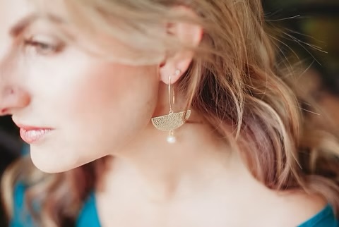 Close-up of a woman with blonde hair wearing a pearl earring and a blue top.