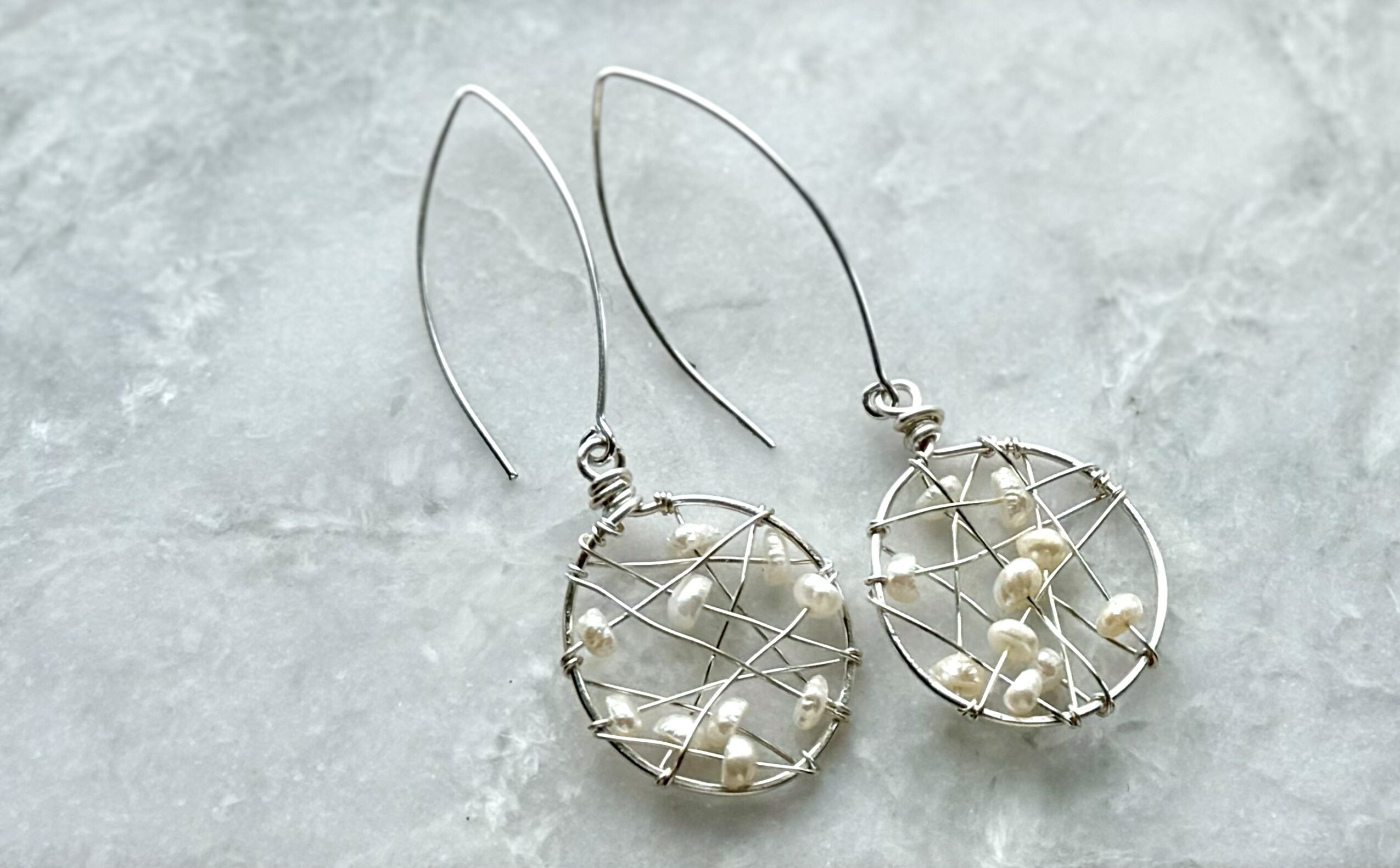 Pair of dangling earrings with wire frames and small pearl-like beads, on a light textured surface.