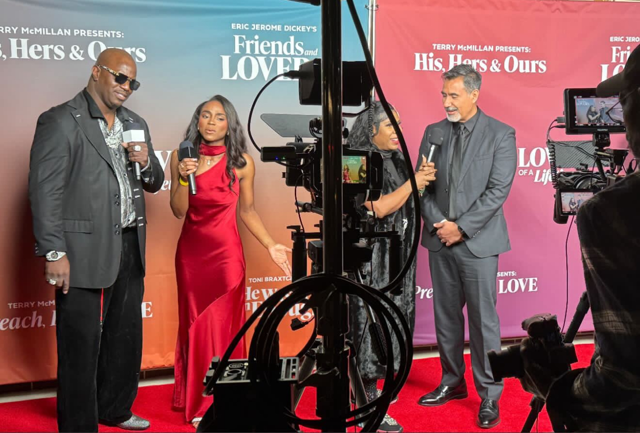 Two men and a woman on a red carpet with cameras and backdrop, holding microphones during an event.