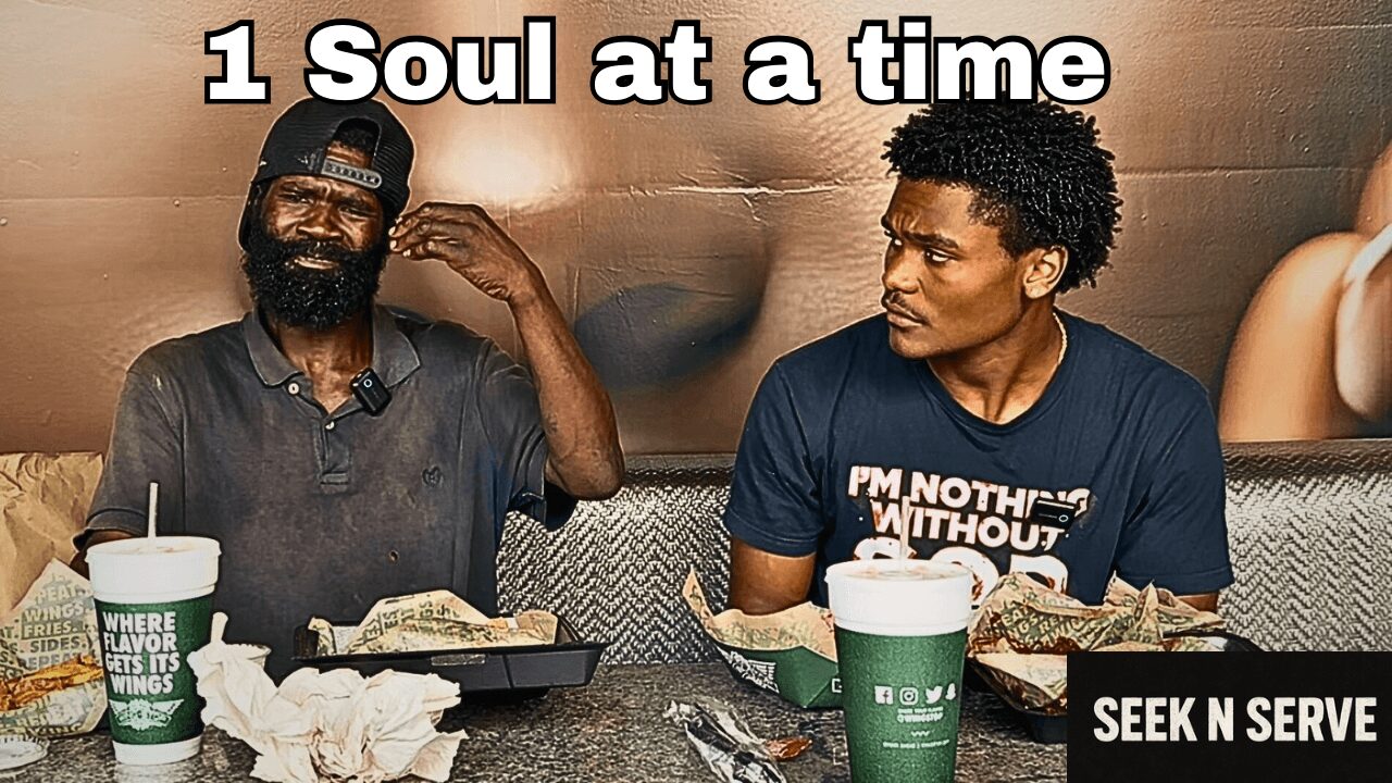Two men sitting at a table with food and drinks, smiling and talking, in a casual setting.
