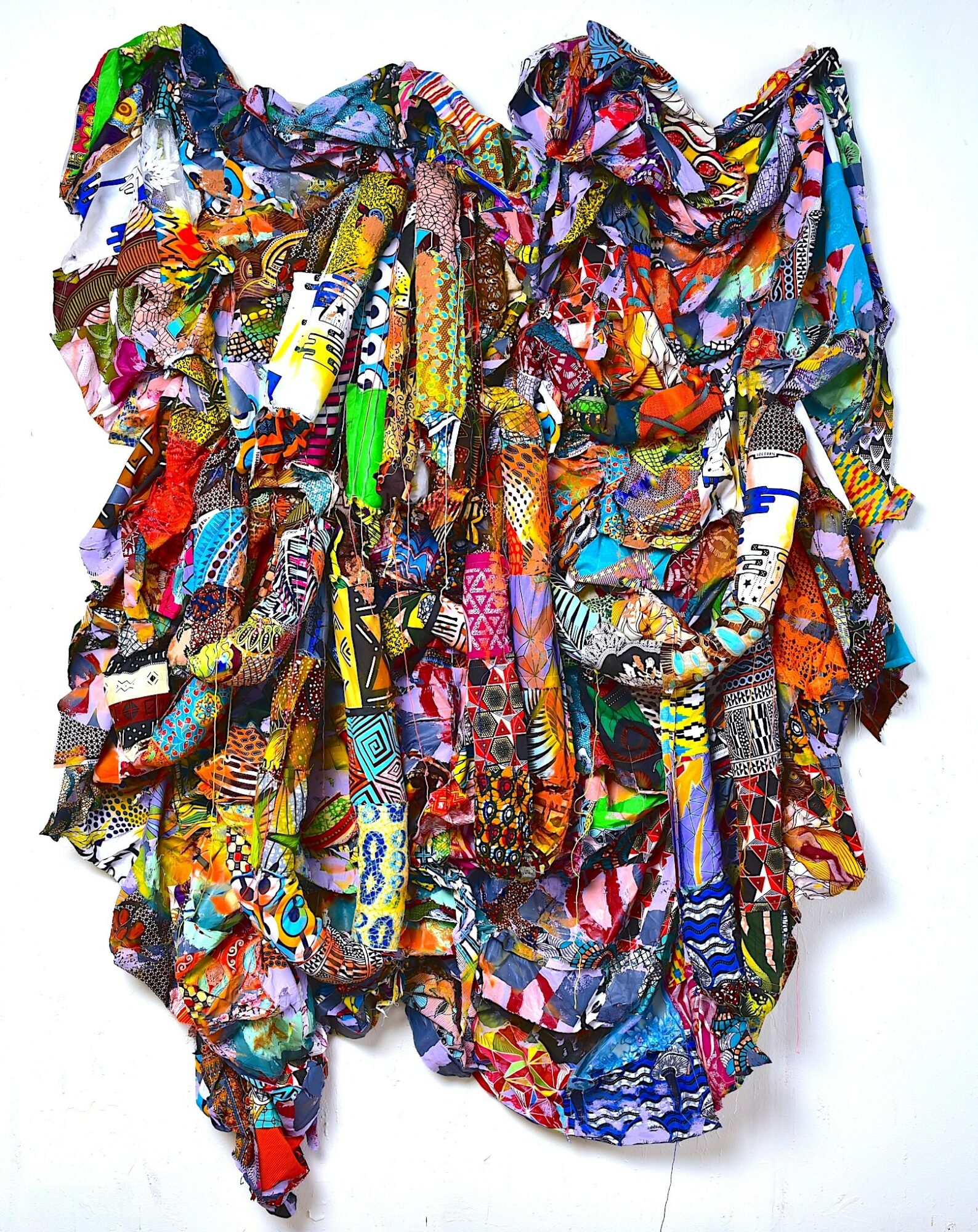 Colorful, ruffled fabric with various patterns and textures, hanging against a white background.